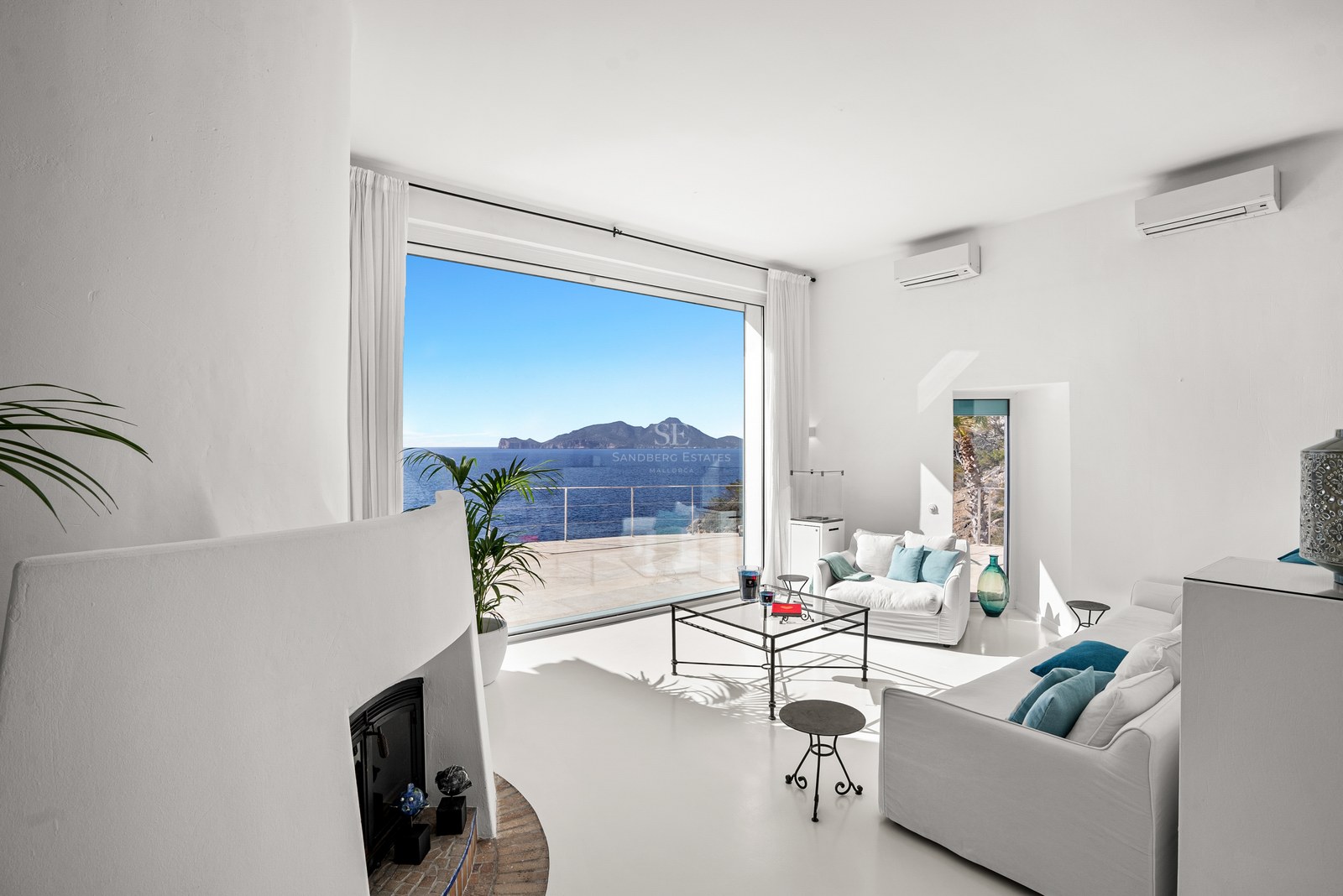 Bright white living room with a large picture window overlooking the Mediterranean sea and a distant island.