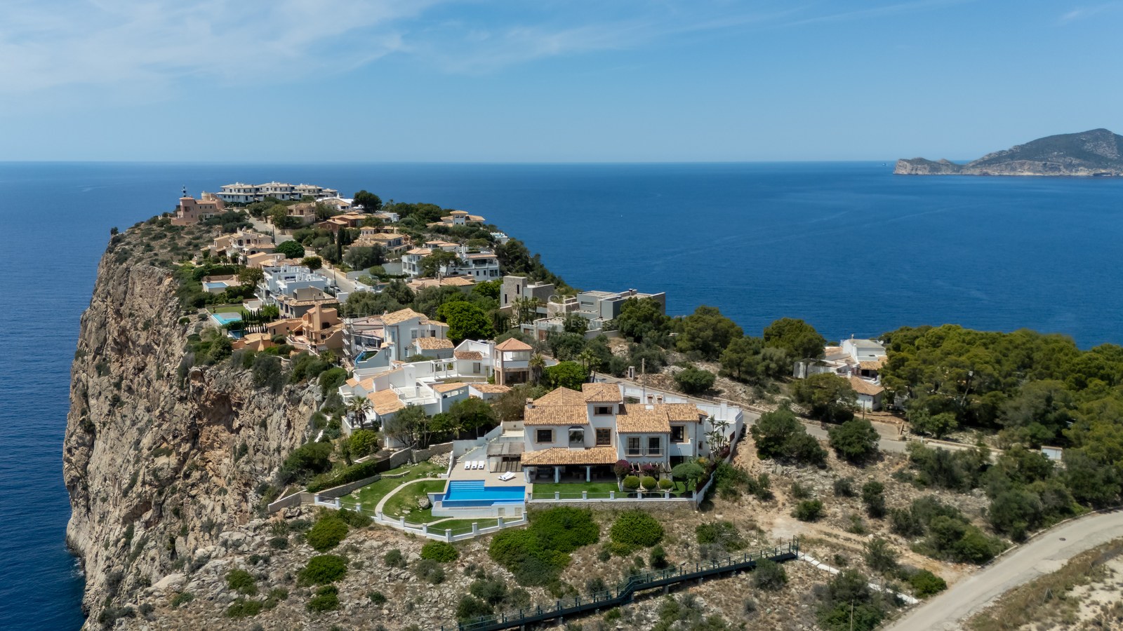 Vue aérienne d'une villa de luxe blanche avec piscine perchée sur une falaise rocheuse surplombant la Méditerranée.