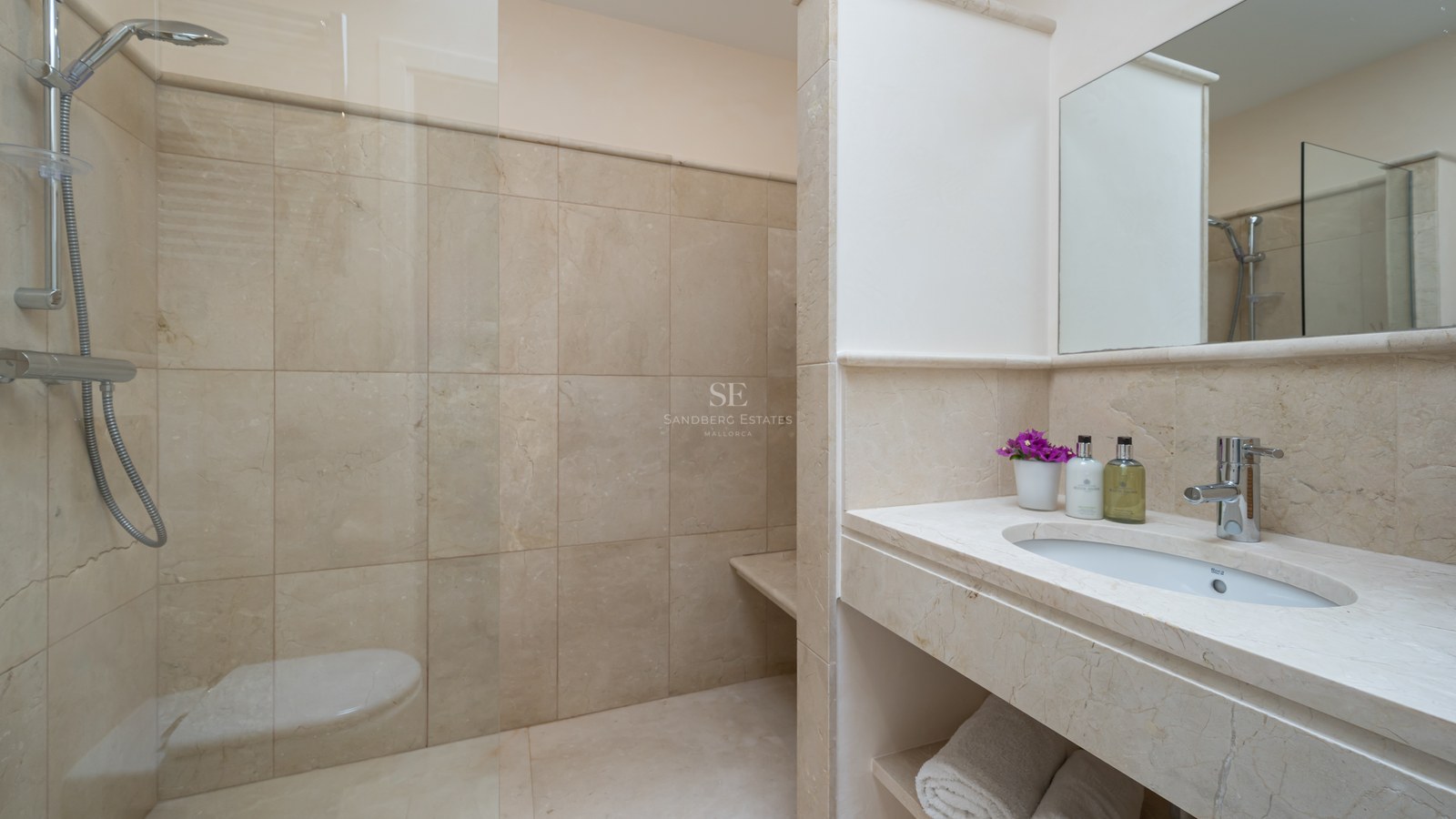Salle de bains moderne avec carrelage en pierre beige, paroi de douche en verre et vasque intégrée en pierre.