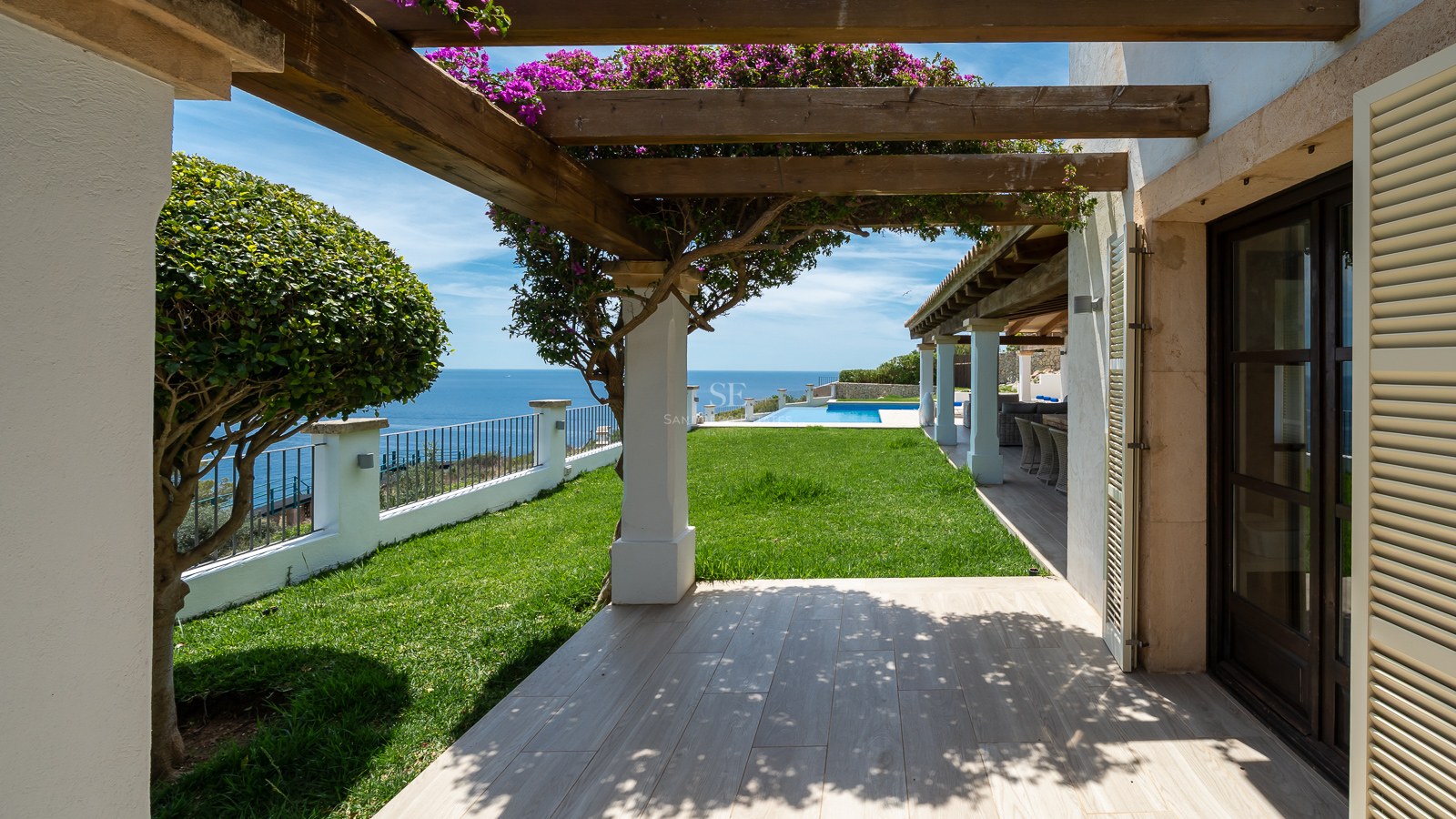 Terrasse ensoleillée avec pergola en bois, bougainvilliers et pelouse offrant une vue sur la mer Méditerranée.