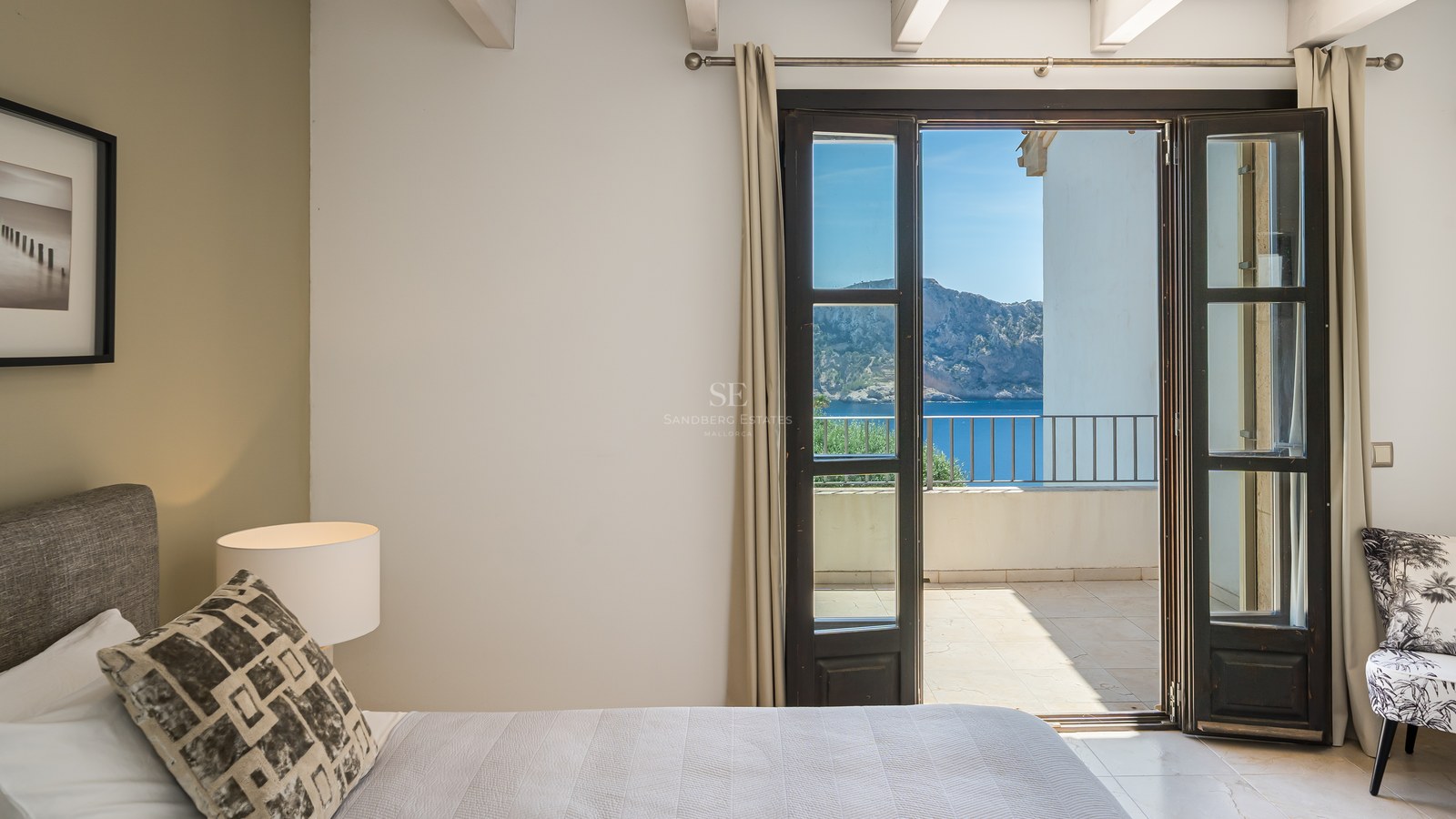 Chambre contemporaine avec poutres blanches et portes-fenêtres ouvrant sur une terrasse avec vue sur la Méditerranée.