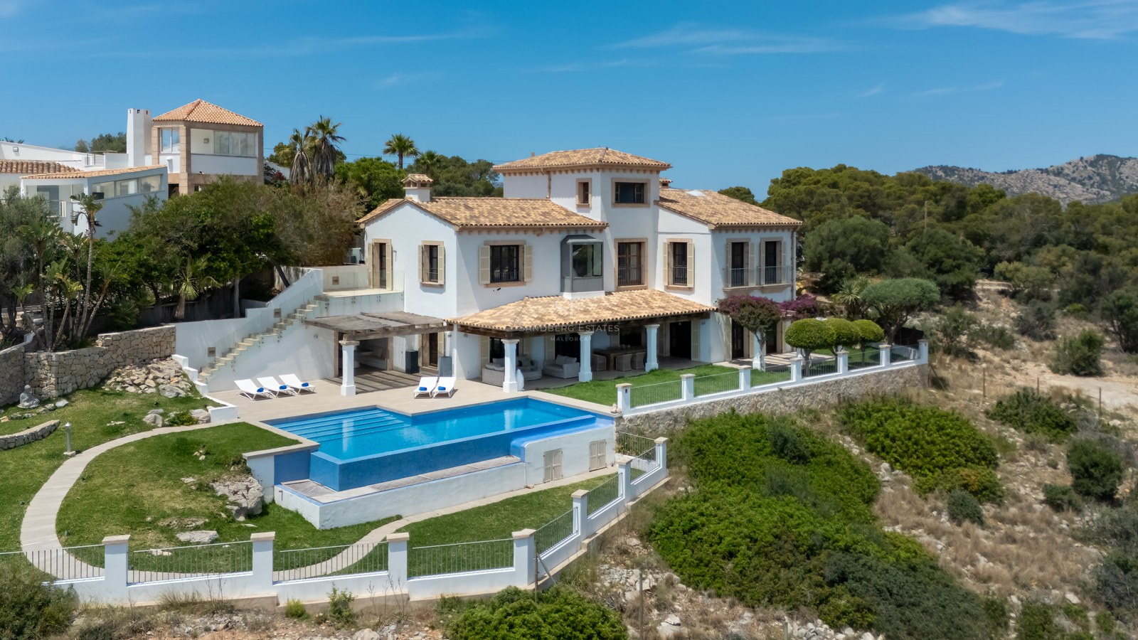 Vue extérieure d'une villa blanche méditerranéenne avec piscine bleue et toit en terre cuite par beau temps.