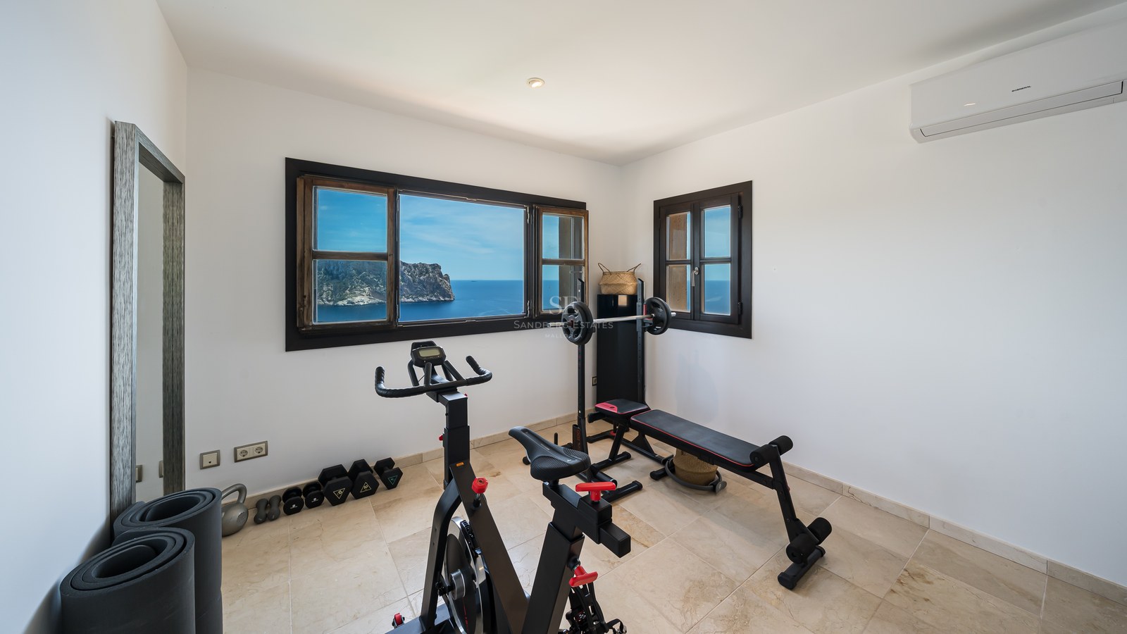 Salle de sport à domicile avec vélo d'appartement et banc de musculation devant une fenêtre donnant sur la mer.