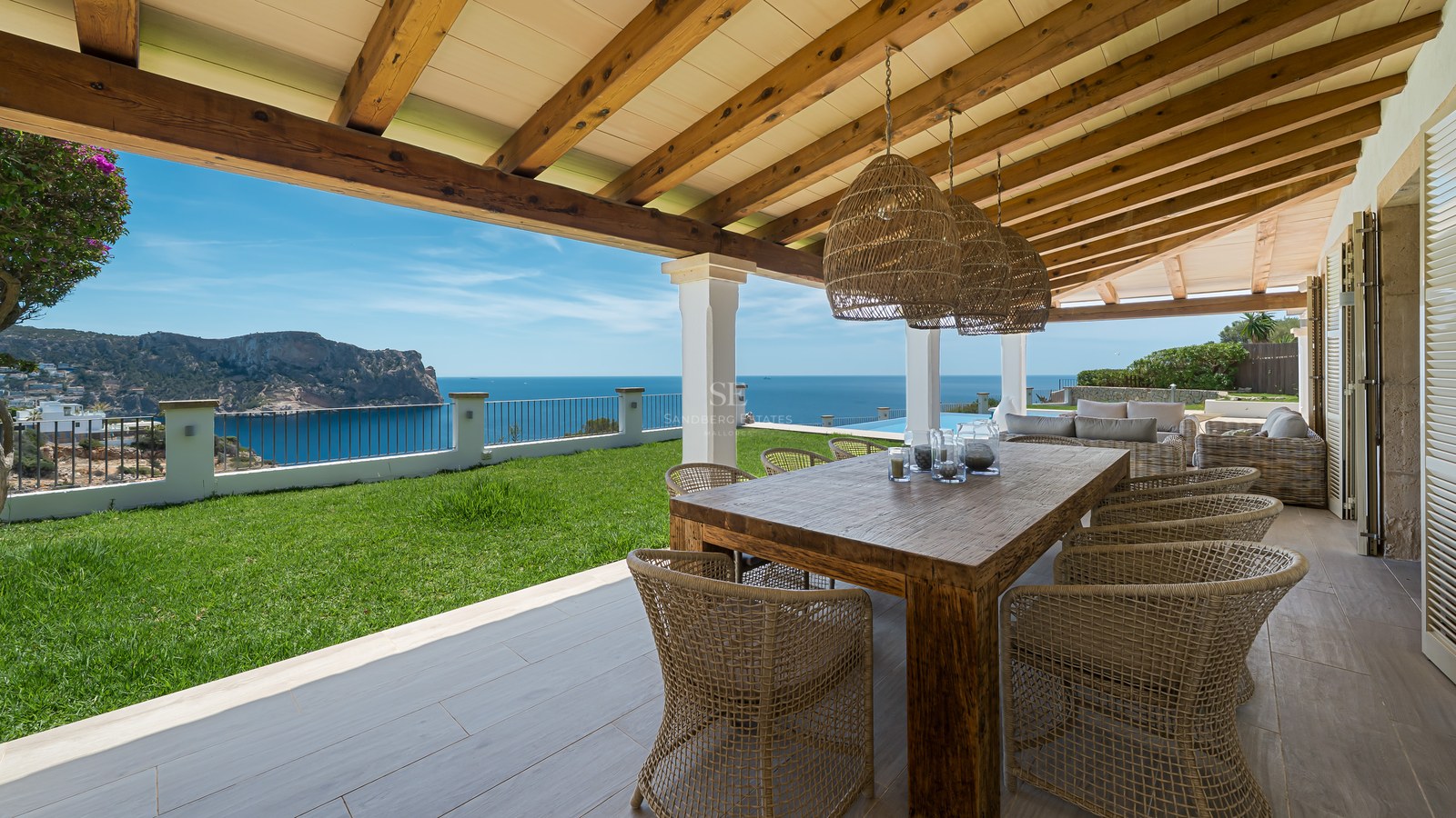Grande table à manger en bois sous une terrasse couverte avec poutres apparentes, surplombant la mer Méditerranée.