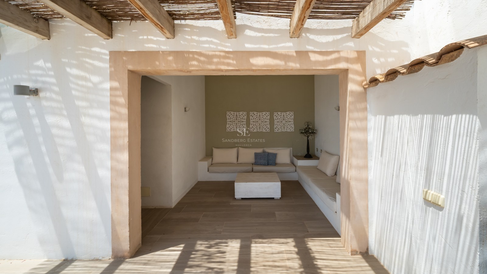 Salon de jardin ombragé avec canapés intégrés sous une pergola en bois et canisse, encadrement en pierre naturelle.