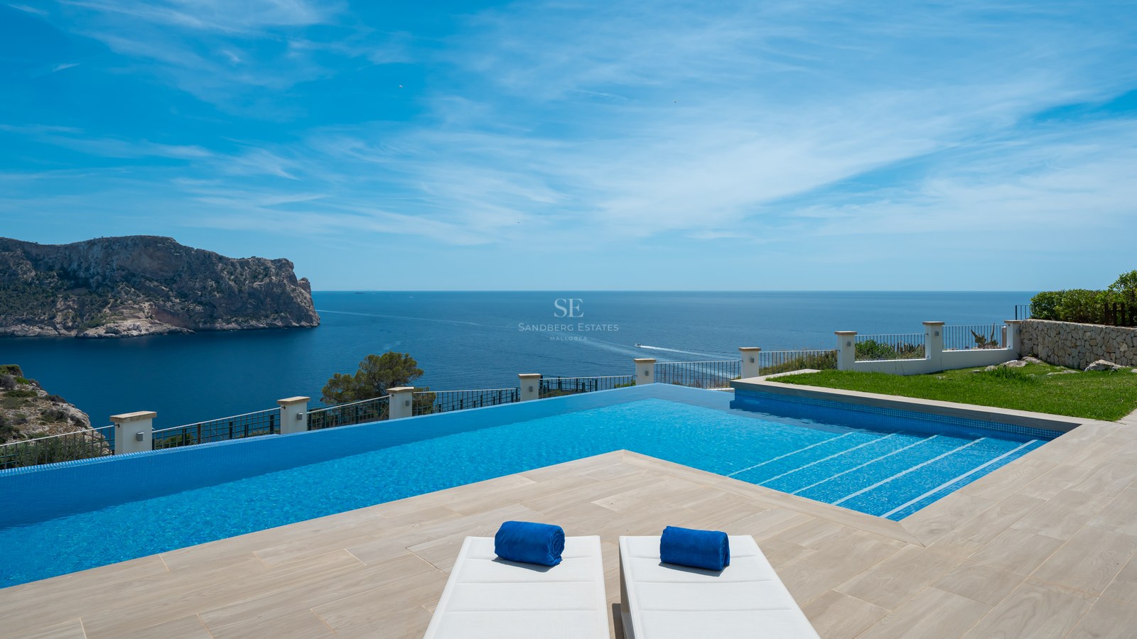 Piscine à débordement surplombant la mer Méditerranée avec une grande falaise rocheuse en arrière-plan sous un ciel bleu.