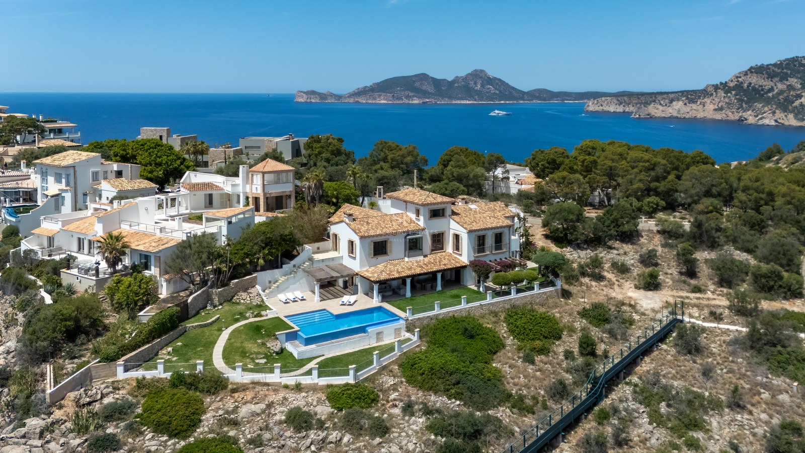 Vue aérienne d'une villa méditerranéenne blanche avec piscine surplombant la mer et les montagnes au loin.