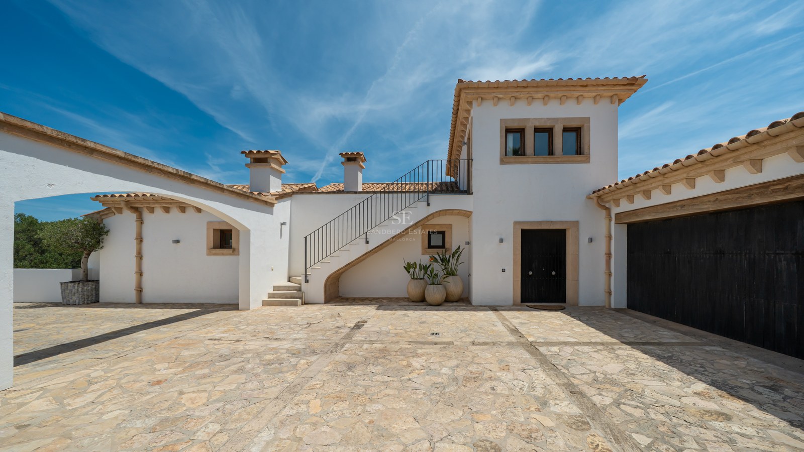 Façade de villa blanche avec cour en pierre naturelle, toit en terre cuite et escalier extérieur par temps clair.