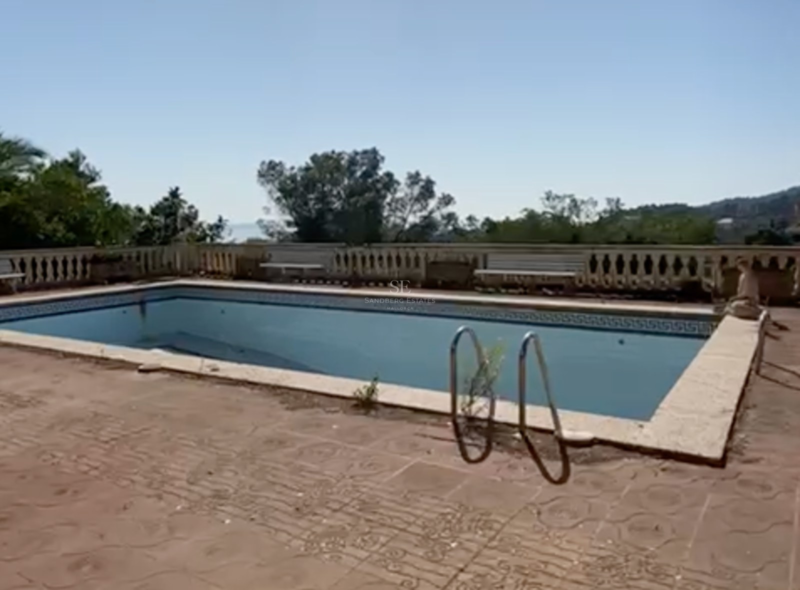 Piscina rectangular exterior con balaustrada de piedra y vistas lejanas al mar bajo un cielo despejado.