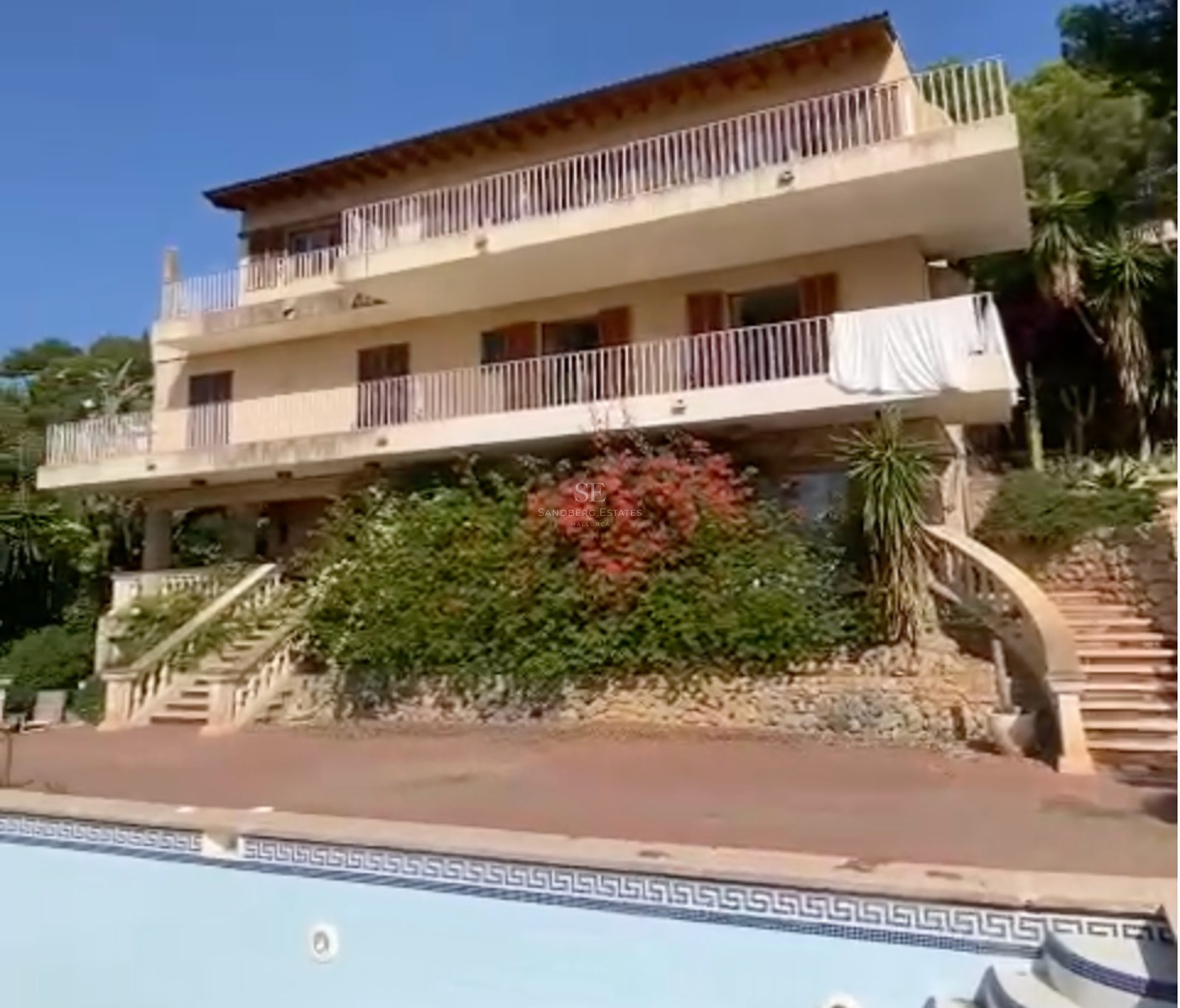 Vista exterior de una villa mediterránea de tres plantas con piscina, terrazas a varios niveles y escaleras de piedra.