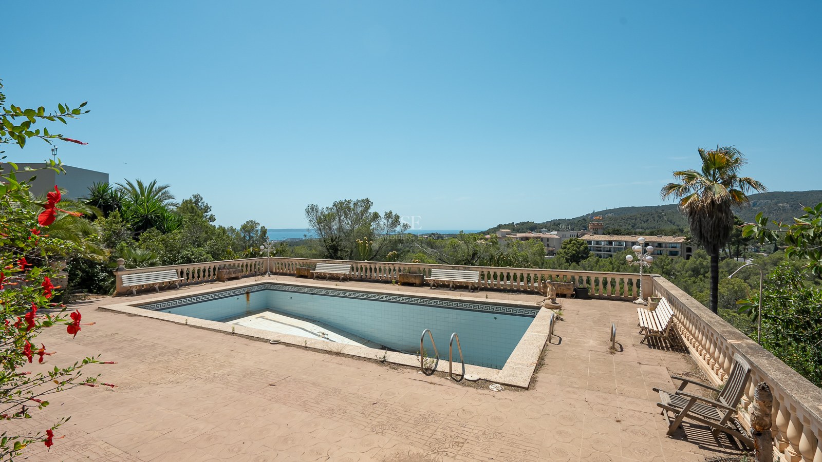 Piscina rectangular vacía en una terraza de terracota con balaustradas de piedra y vistas lejanas al mar.