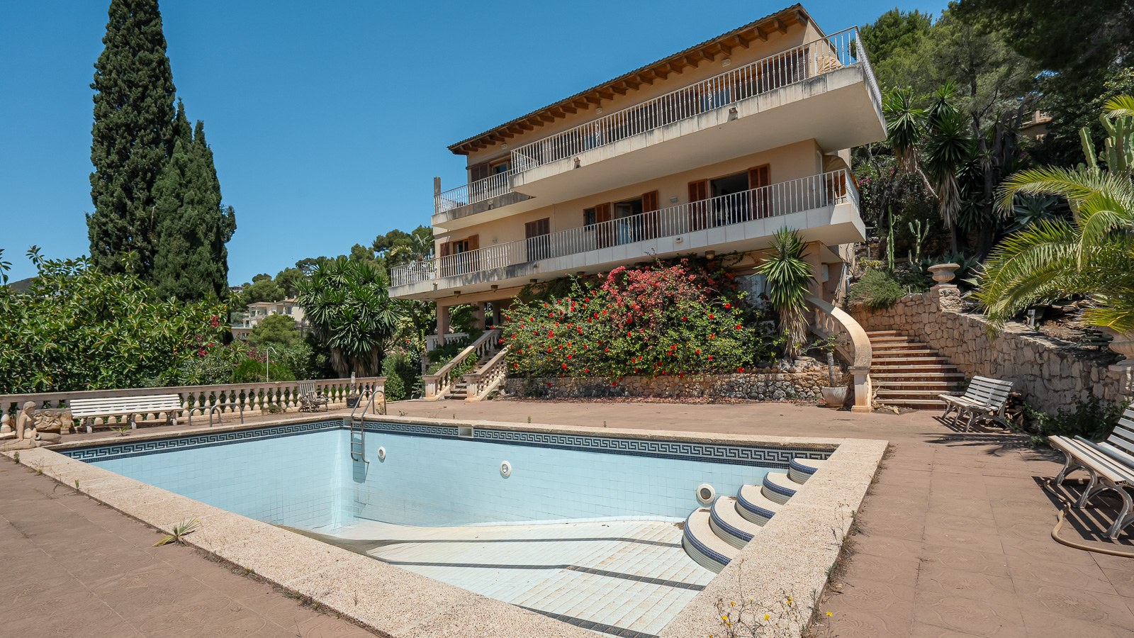 Gran piscina privada frente a una villa mediterránea de tres niveles con terrazas y jardines consolidados.