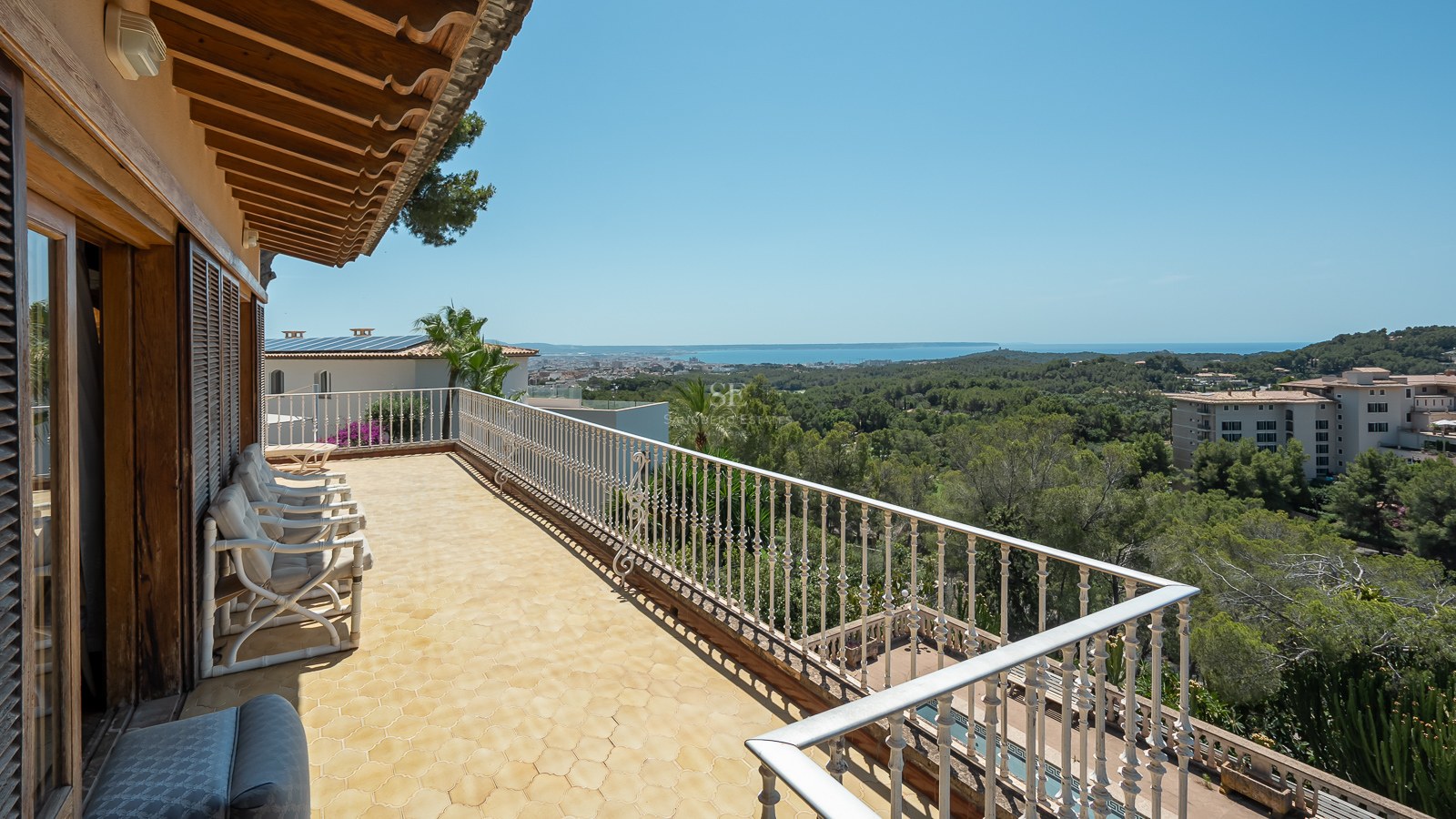 Terraza mediterránea con baldosas de terracota y barandilla blanca con vistas a un bosque de pinos y al mar.