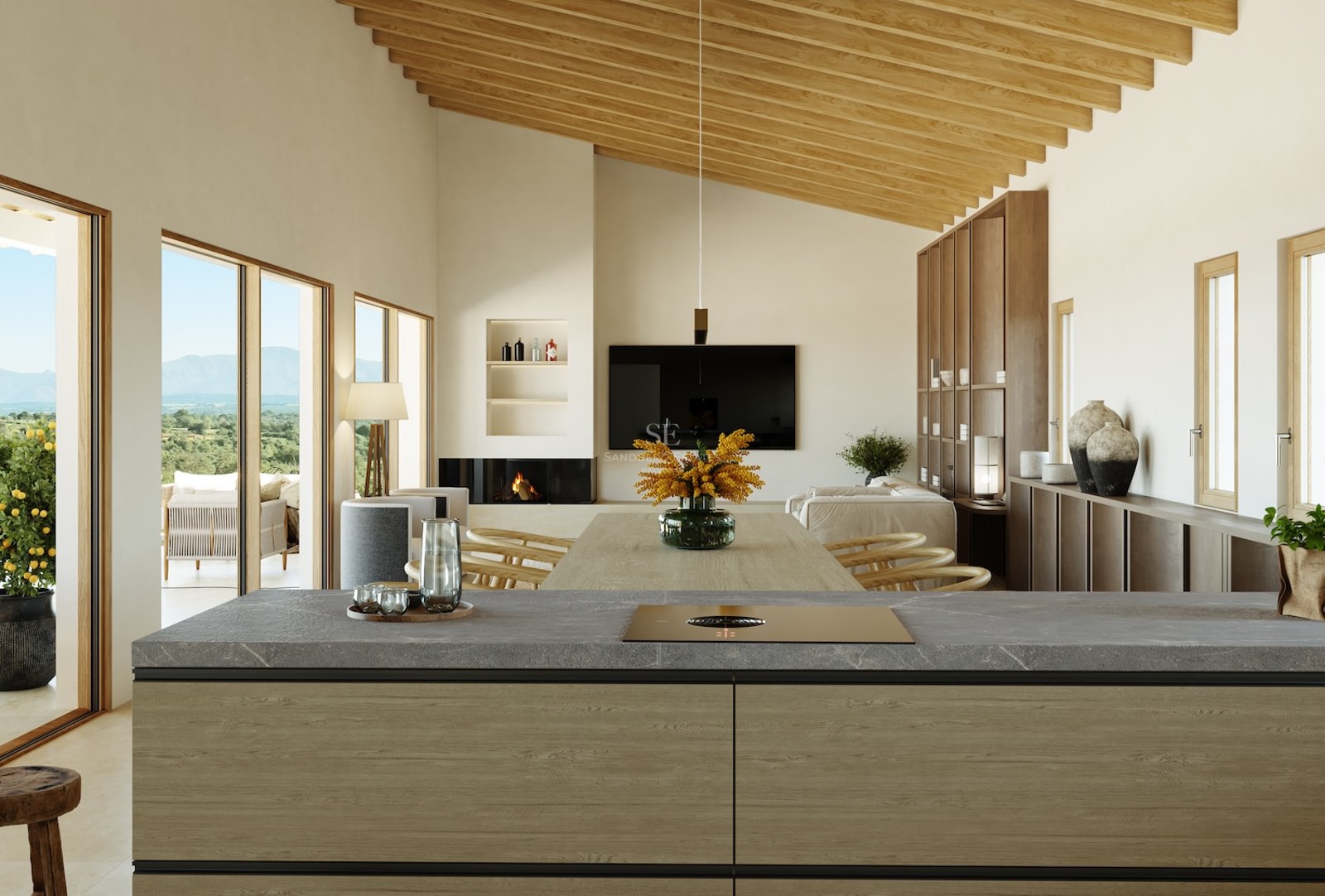 Innenansicht von der Kücheninsel zum Wohnzimmer mit Holzbalken, Kamin und großen Fenstern mit Landschaftsblick.