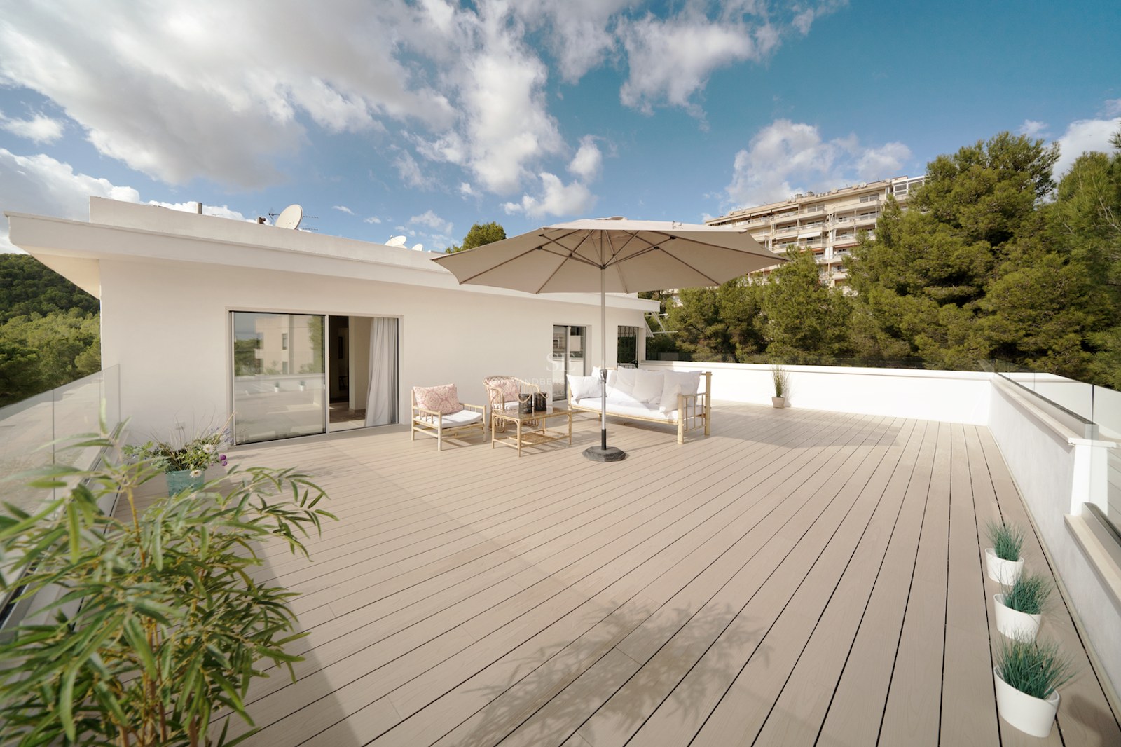 Terraza espaciosa con tarima de madera, muebles de exterior blancos y barandillas de cristal bajo un cielo despejado.