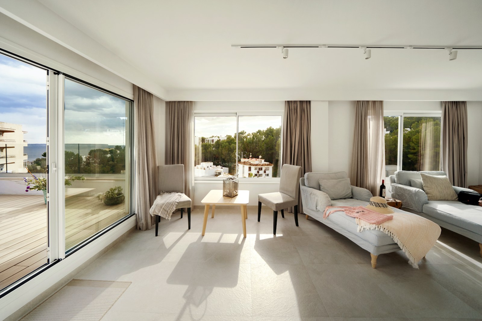 Salón contemporáneo lleno de luz natural con grandes ventanales y acceso a terraza con vistas al mar.