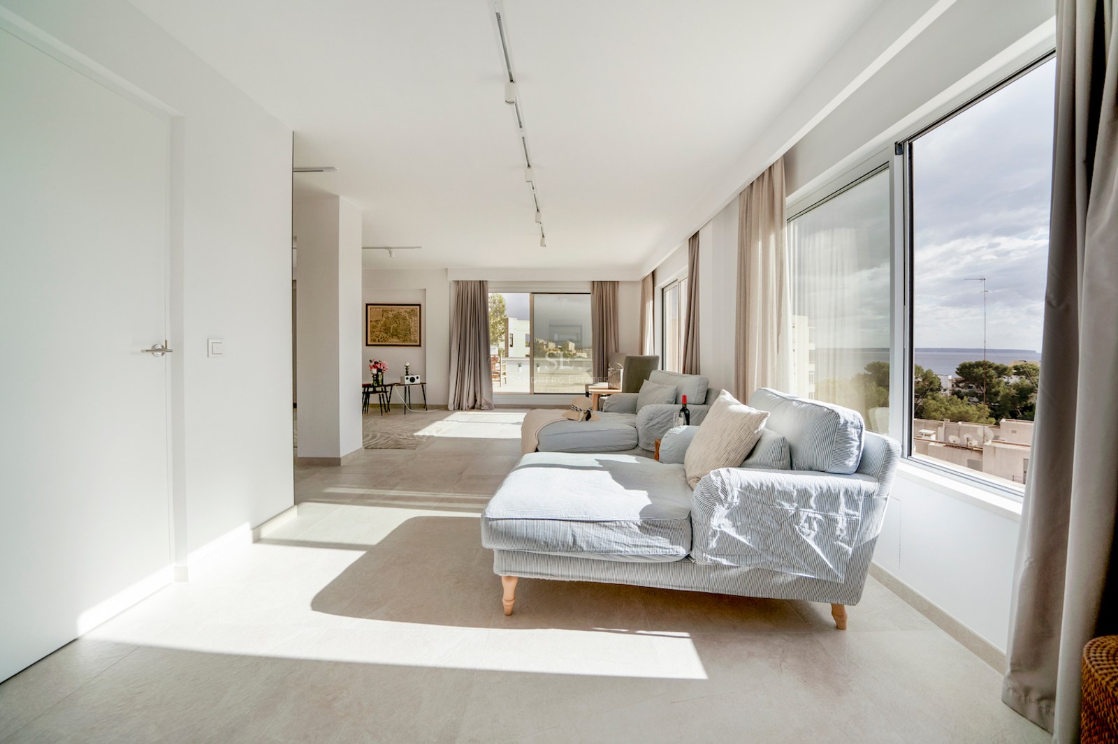 Salón moderno con sofás a rayas azul claro y grandes ventanales con vistas al mar y la costa mediterránea.