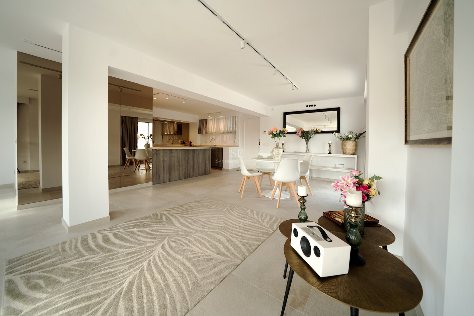 Espacio interior luminoso con comedor blanco, isla de madera, espejos de pared y suelos de gres porcelánico claro.
