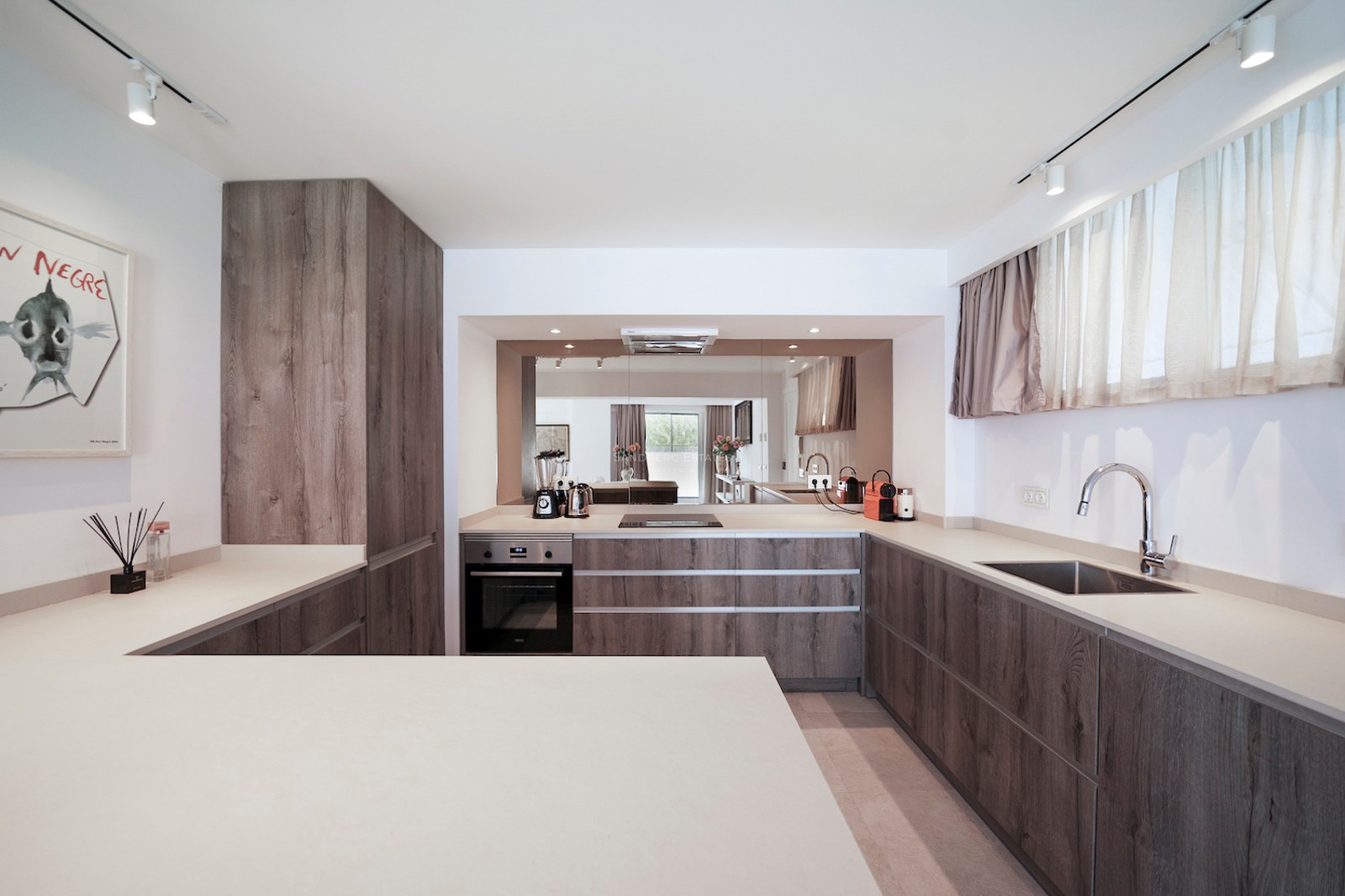 Cocina minimalista con armarios de madera oscura, encimeras blancas y rieles de iluminación modernos.