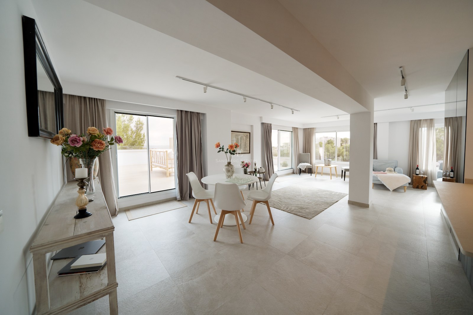 Comedor moderno con muebles blancos, suelos de porcelánico claro y grandes ventanales que dan a una terraza exterior.