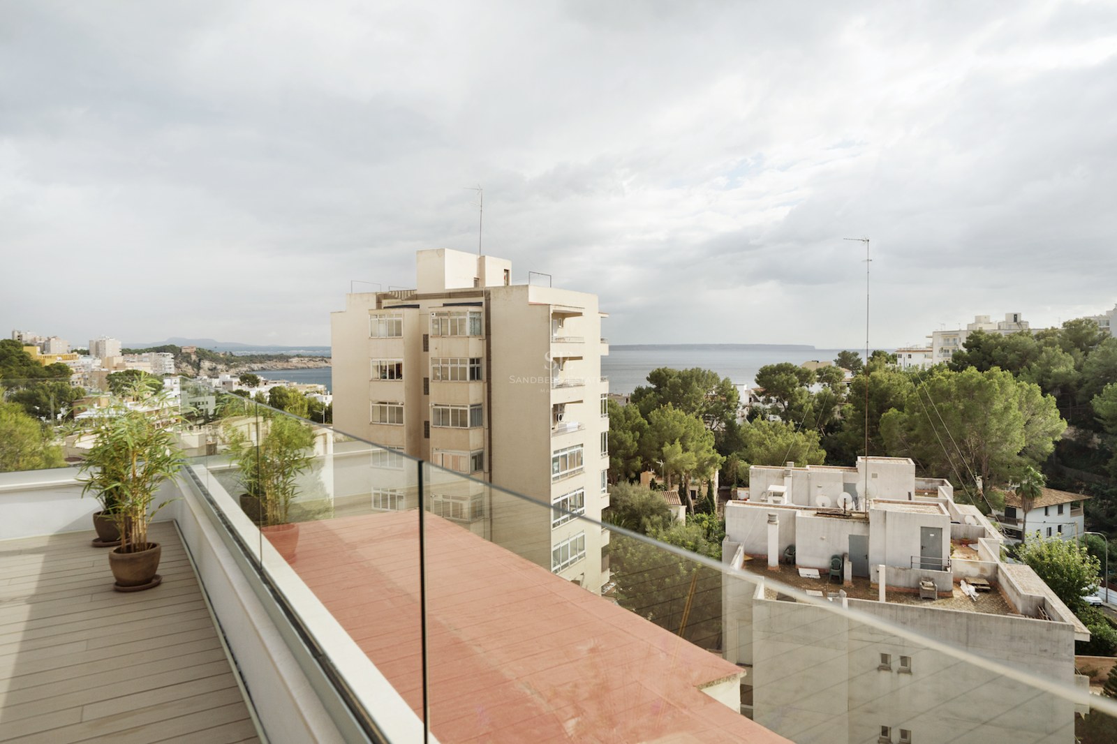 Terraza contemporánea con suelo de madera y barandillas de cristal con vistas a la ciudad y al mar Mediterráneo.