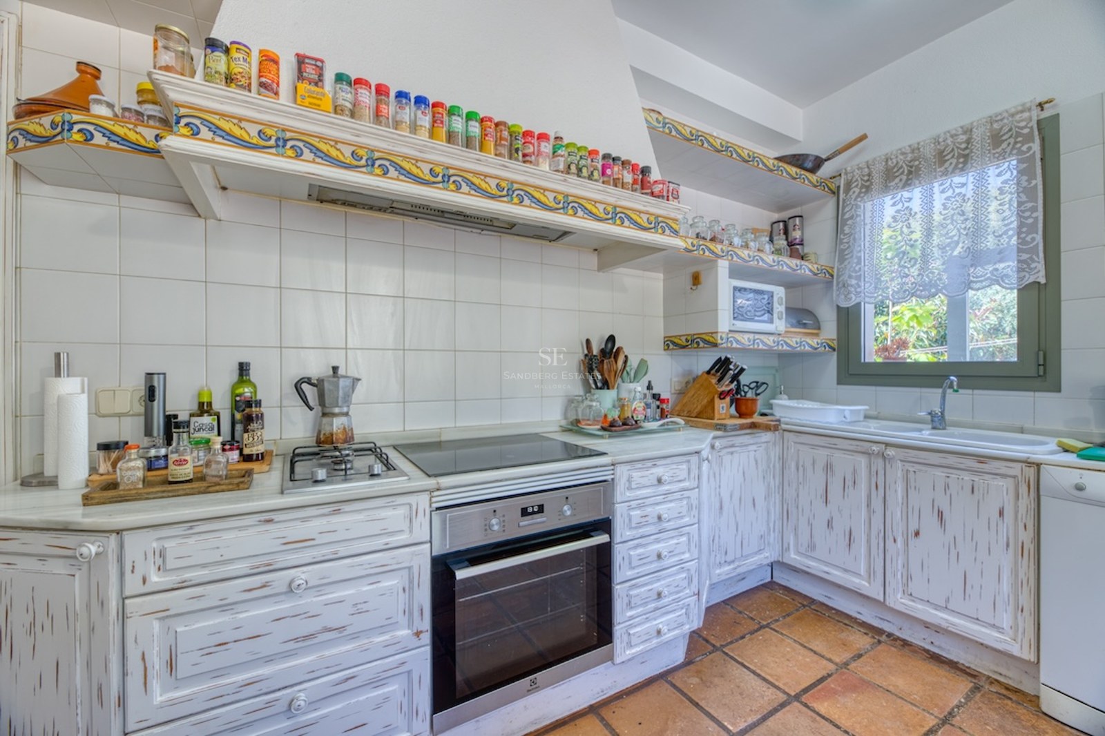 Cuisine de style méditerranéen avec meubles en bois blanchi, sol en terre cuite et bordures en céramique.
