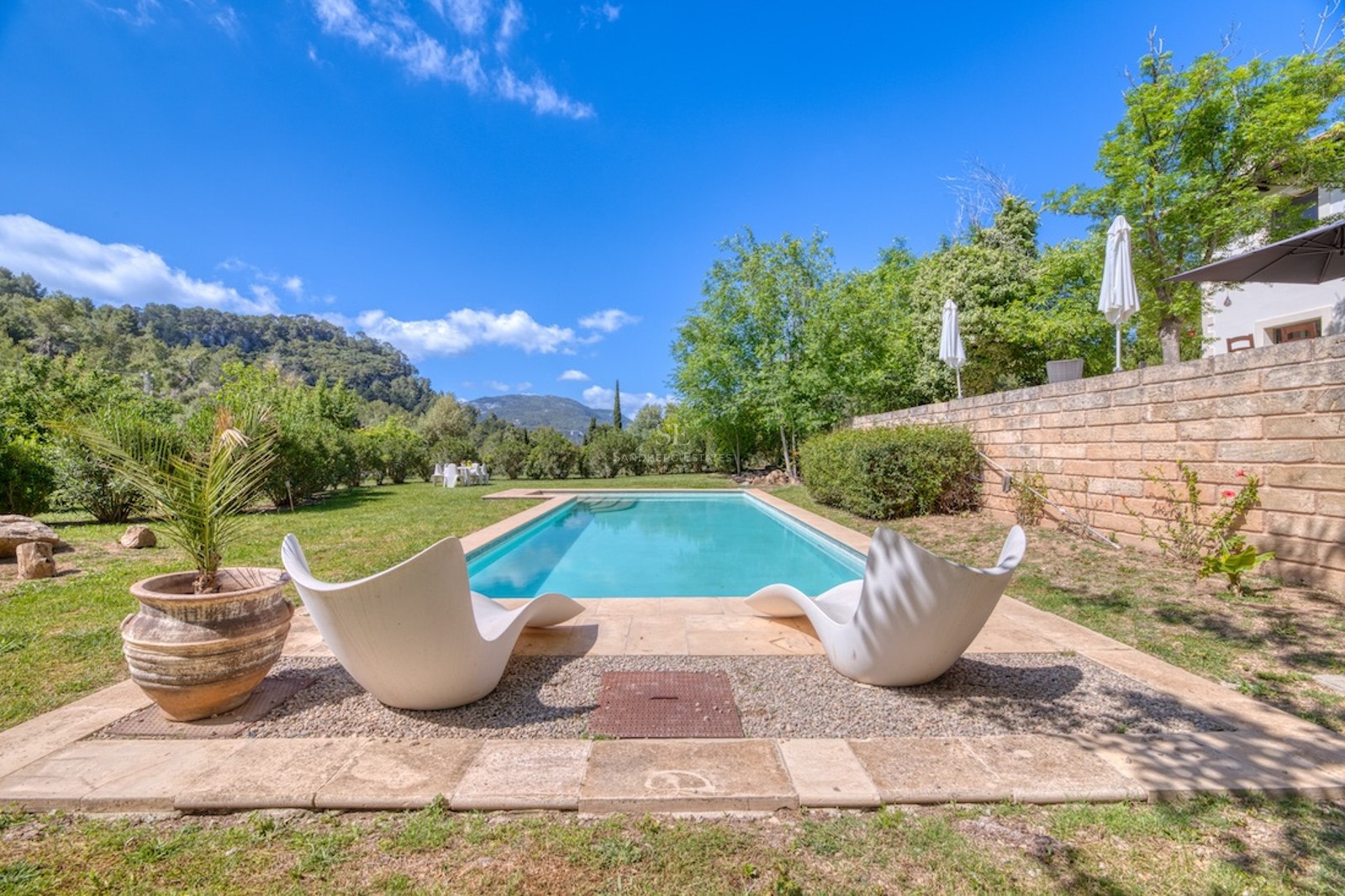 Piscine rectangulaire entourée d'une terrasse en pierre, pelouse verte, deux chaises longues blanches et vue montagne.