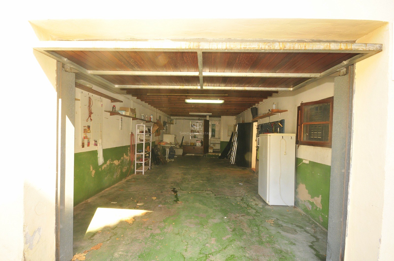 Interiör av ett rymligt garage med grönt betonggolv, trätak och förvaringshyllor.