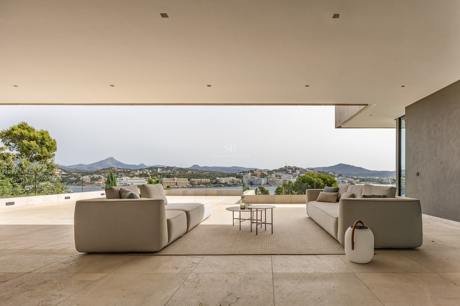 Contemporary covered terrace with neutral-toned sofas and an expansive view of the coastline and mountains.