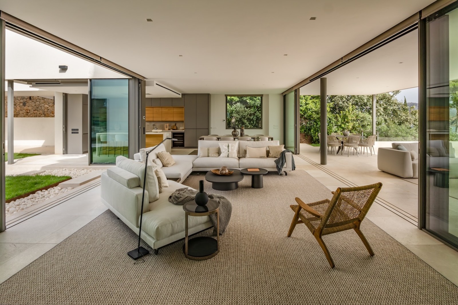 Spacious contemporary living room with cream sofas and glass walls opening onto a terrace and lush garden.