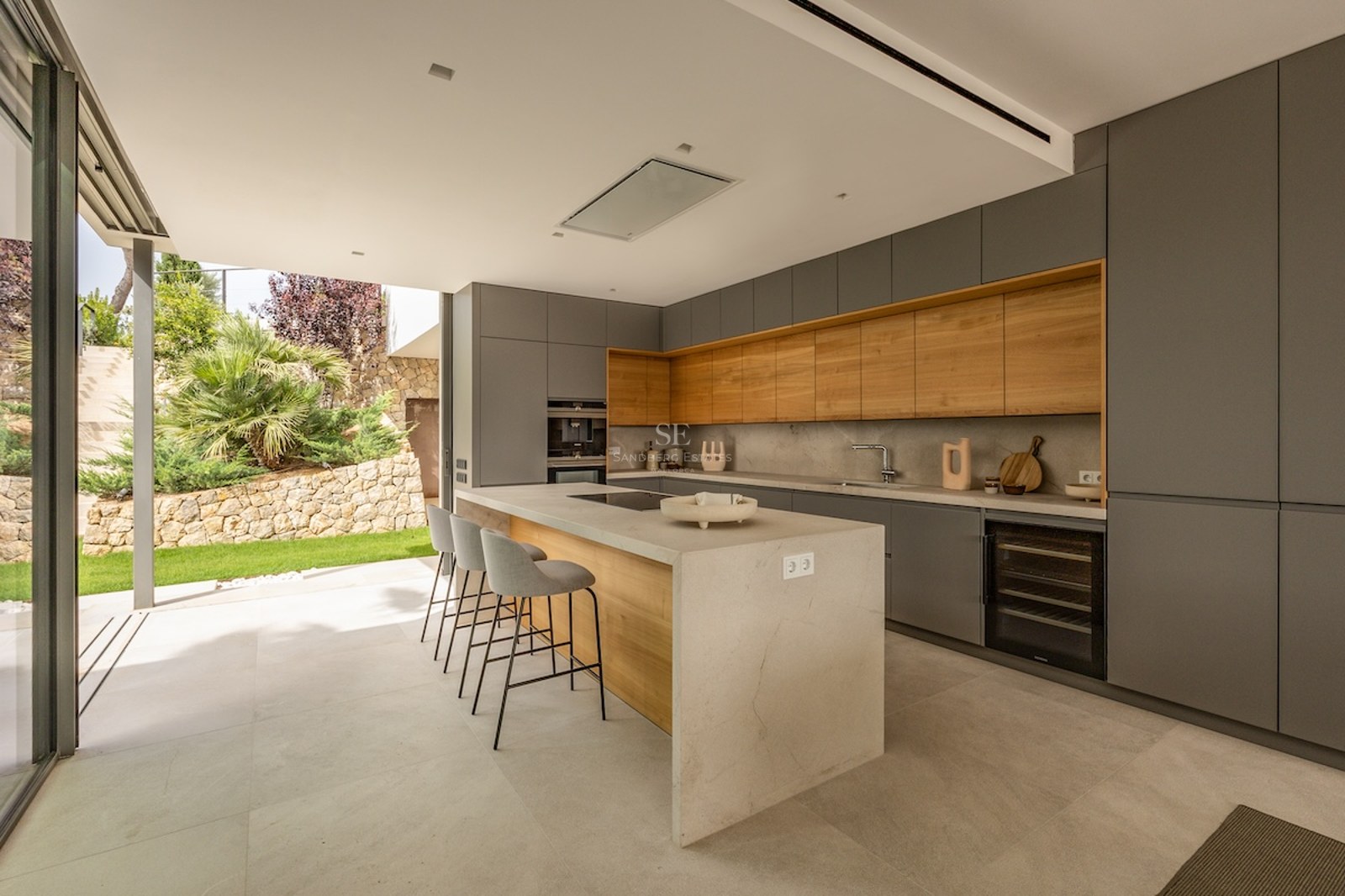 Modern grey and wood kitchen featuring a large central island with seating and direct access to the garden.