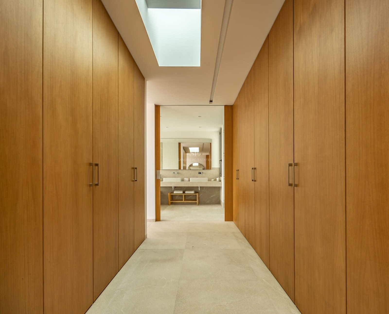 A symmetrical hallway of floor-to-ceiling oak wardrobes lit by a rectangular skylight leading to a bathroom.