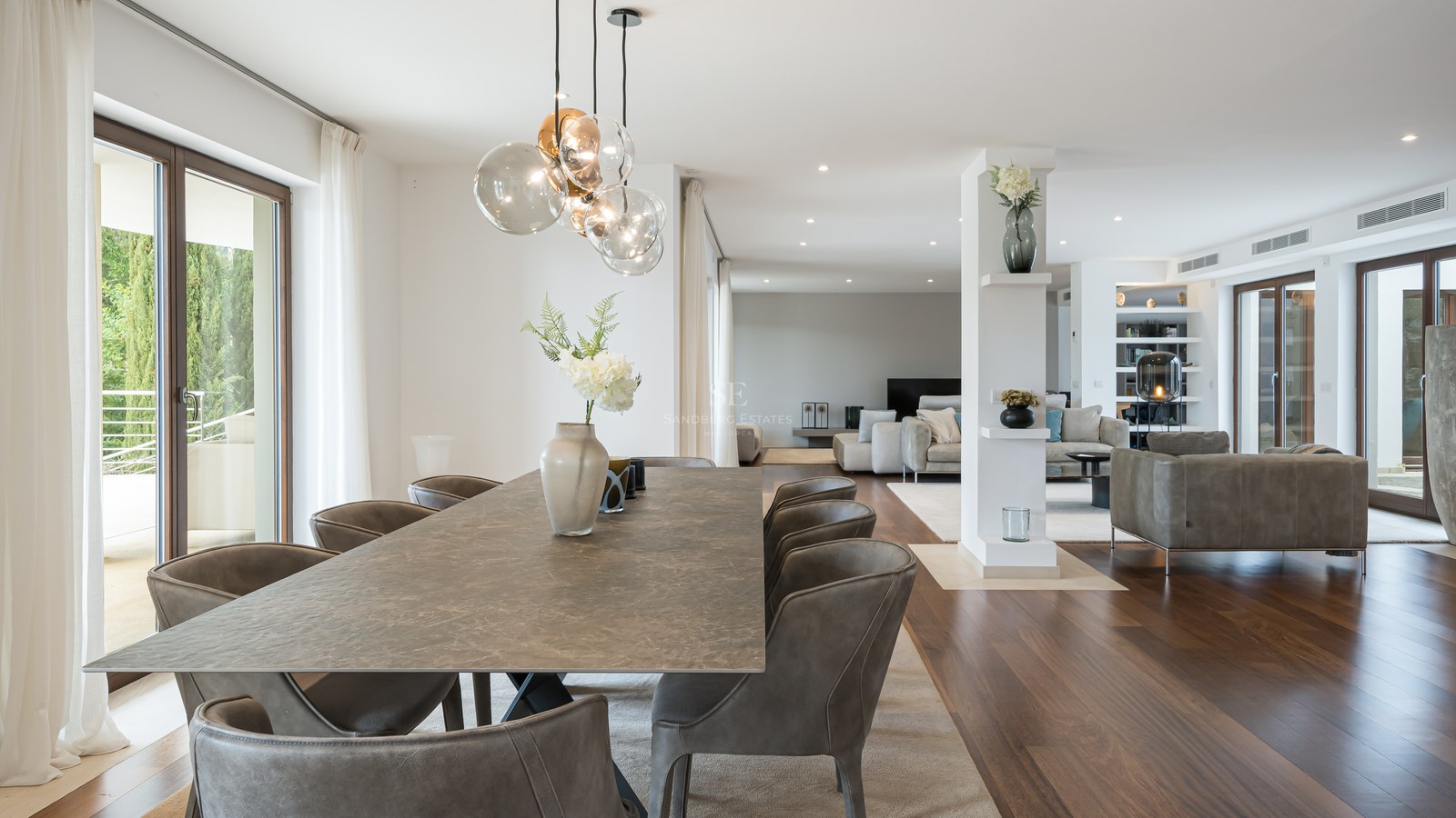 Mesa de comedor de piedra con sillas de cuero en una estancia luminosa con suelos de madera y puertas acristaladas.
