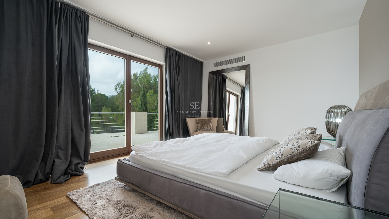 Dormitorio principal contemporáneo con cama blanca, cortinas antracita y puertas de cristal hacia una terraza con vistas.