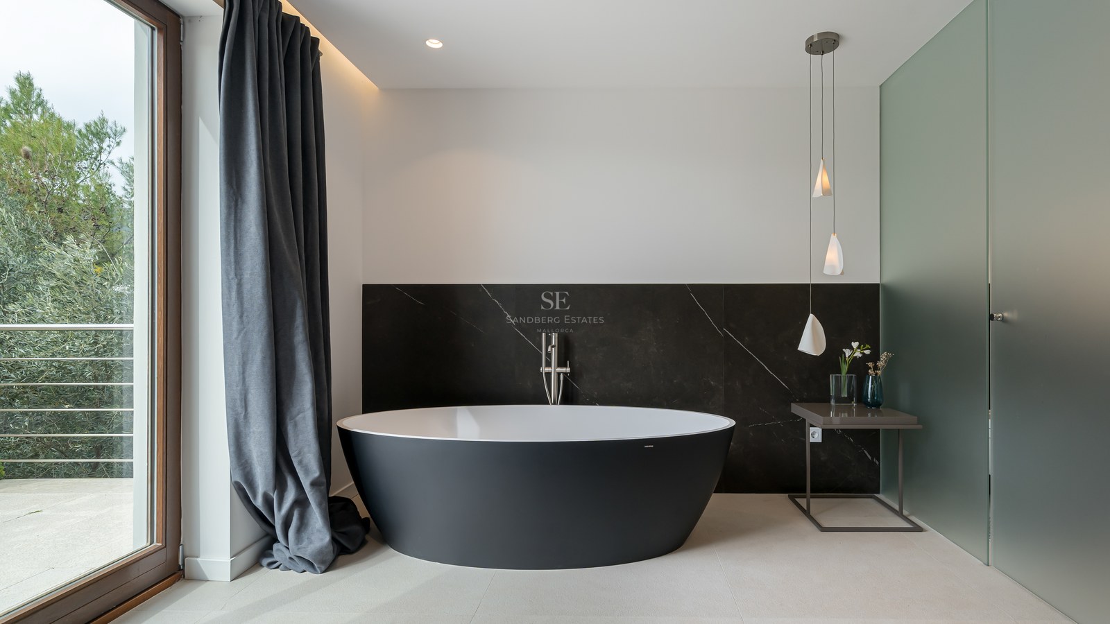 Baño principal moderno con bañera ovalada negra exenta frente a pared de mármol oscuro y luz natural.