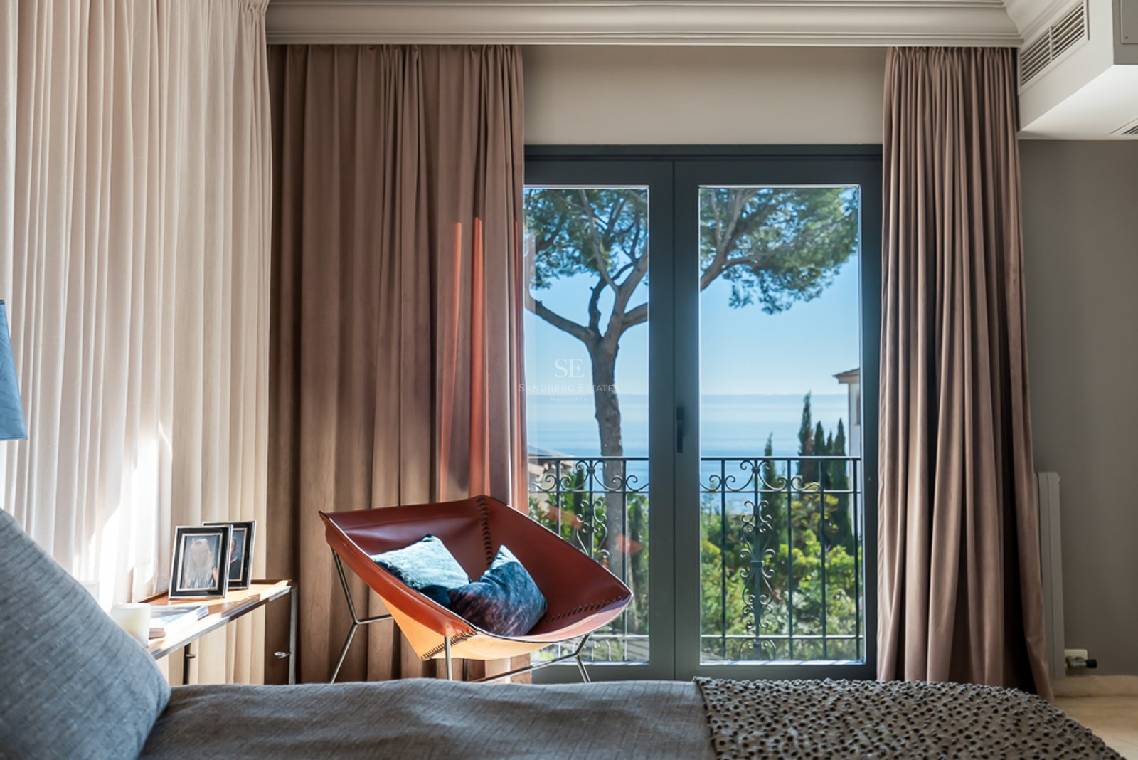 Dormitorio con sillón de cuero frente a ventanales con vistas al mar Mediterráneo y pinos.