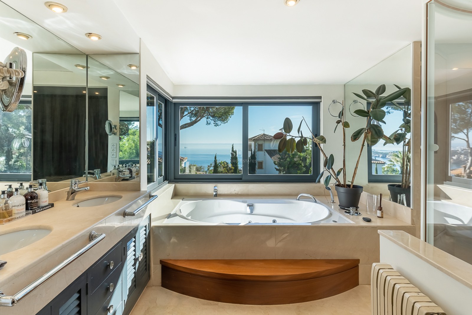 Baño de lujo con bañera de hidromasaje bajo una ventana con vistas panorámicas al mar Mediterráneo y tocador de mármol.