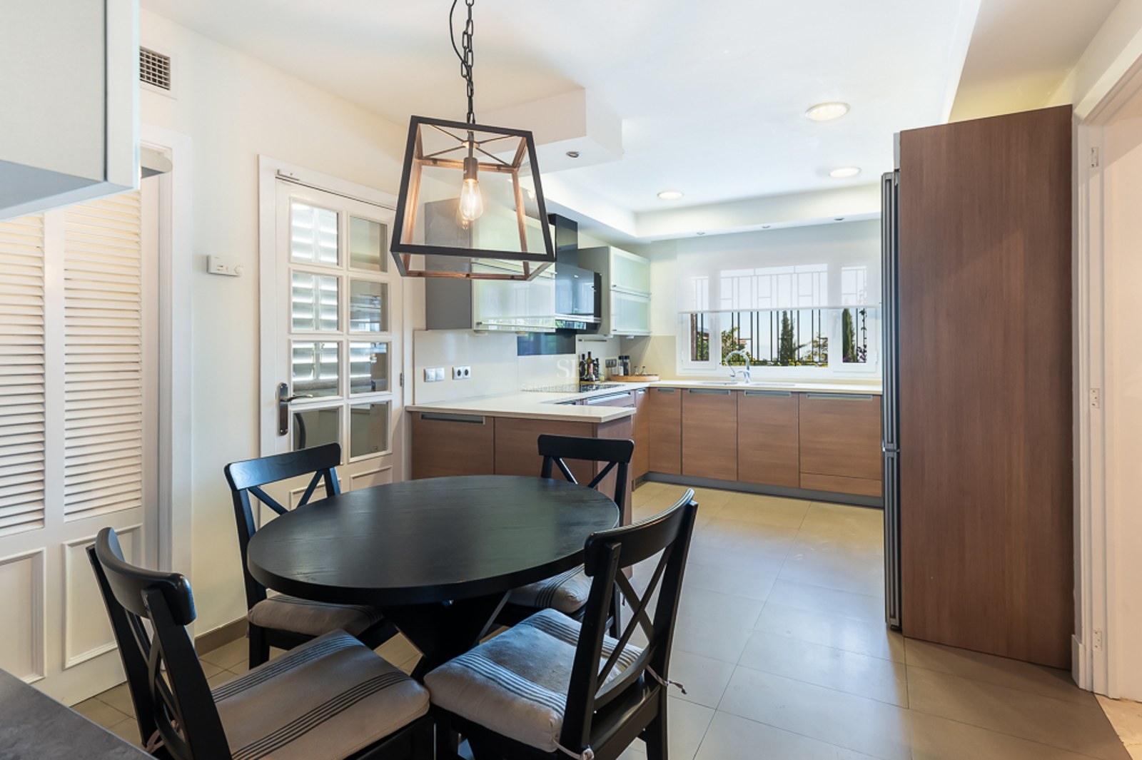Cocina contemporánea con armarios de madera, encimeras blancas y mesa de comedor redonda negra con cuatro sillas.