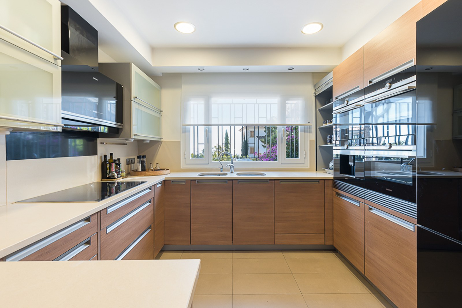 Cocina moderna con armarios de madera, encimeras blancas, electrodomésticos Siemens integrados y ventana al jardín.