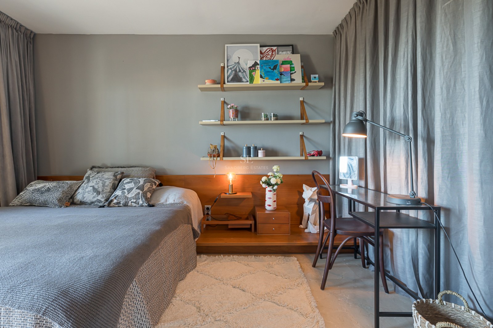 Dormitorio con ropa de cama gris, estanterías de madera integradas, escritorio de metal negro y cortinas grises.