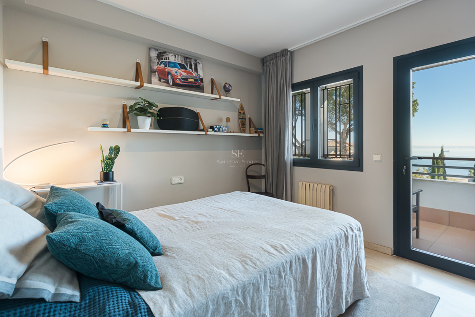 Dormitorio moderno con paredes grises, ropa de cama de lino, estanterías de diseño y puerta hacia un balcón con mar.