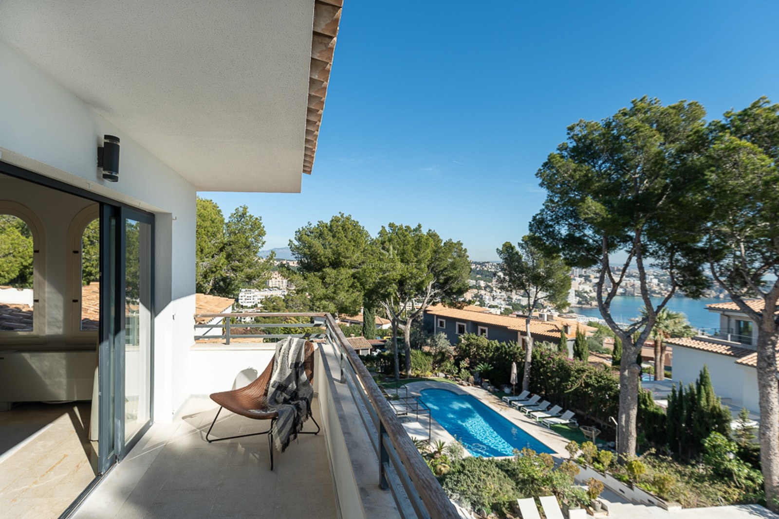 Balcón moderno con silla de diseño y vistas a una piscina, pinos y el mar Mediterráneo en Mallorca.