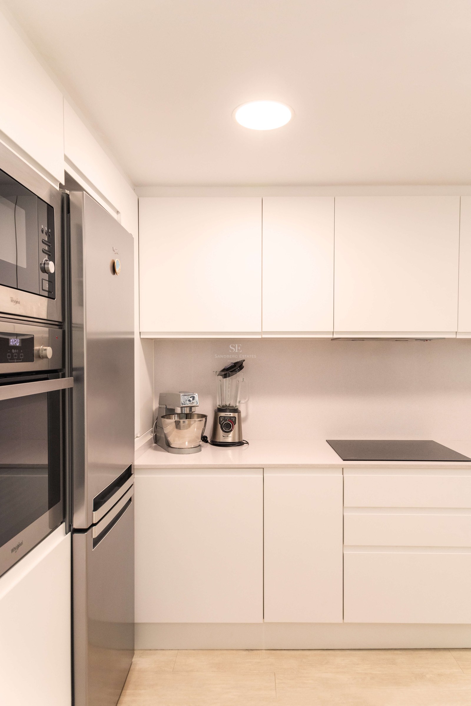 Cuisine blanche minimaliste, appareils en acier inoxydable, plan de travail en pierre et placards sans poignées.
