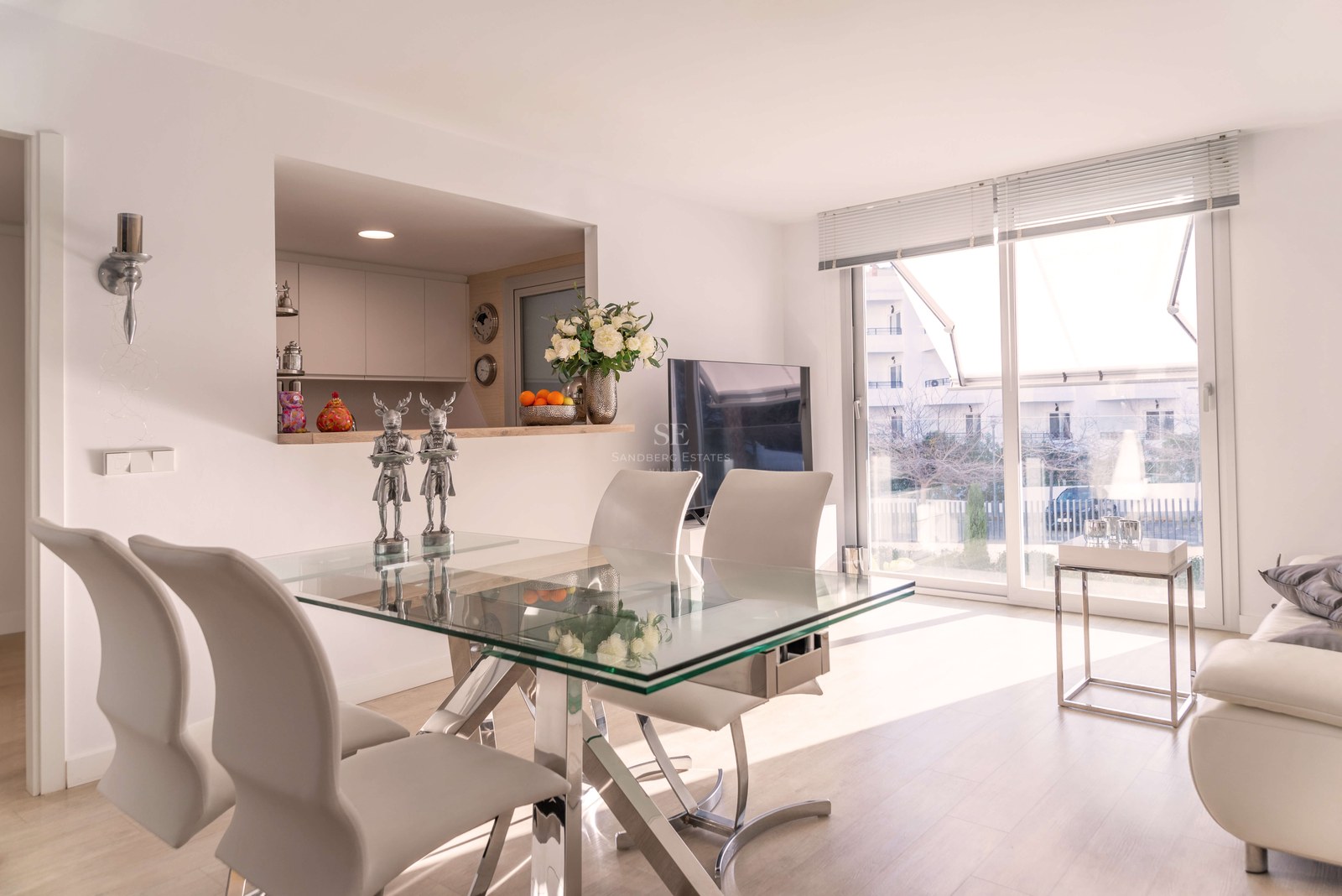 Espace salle à manger contemporain avec table en verre, chaises en cuir blanc et grandes baies vitrées.