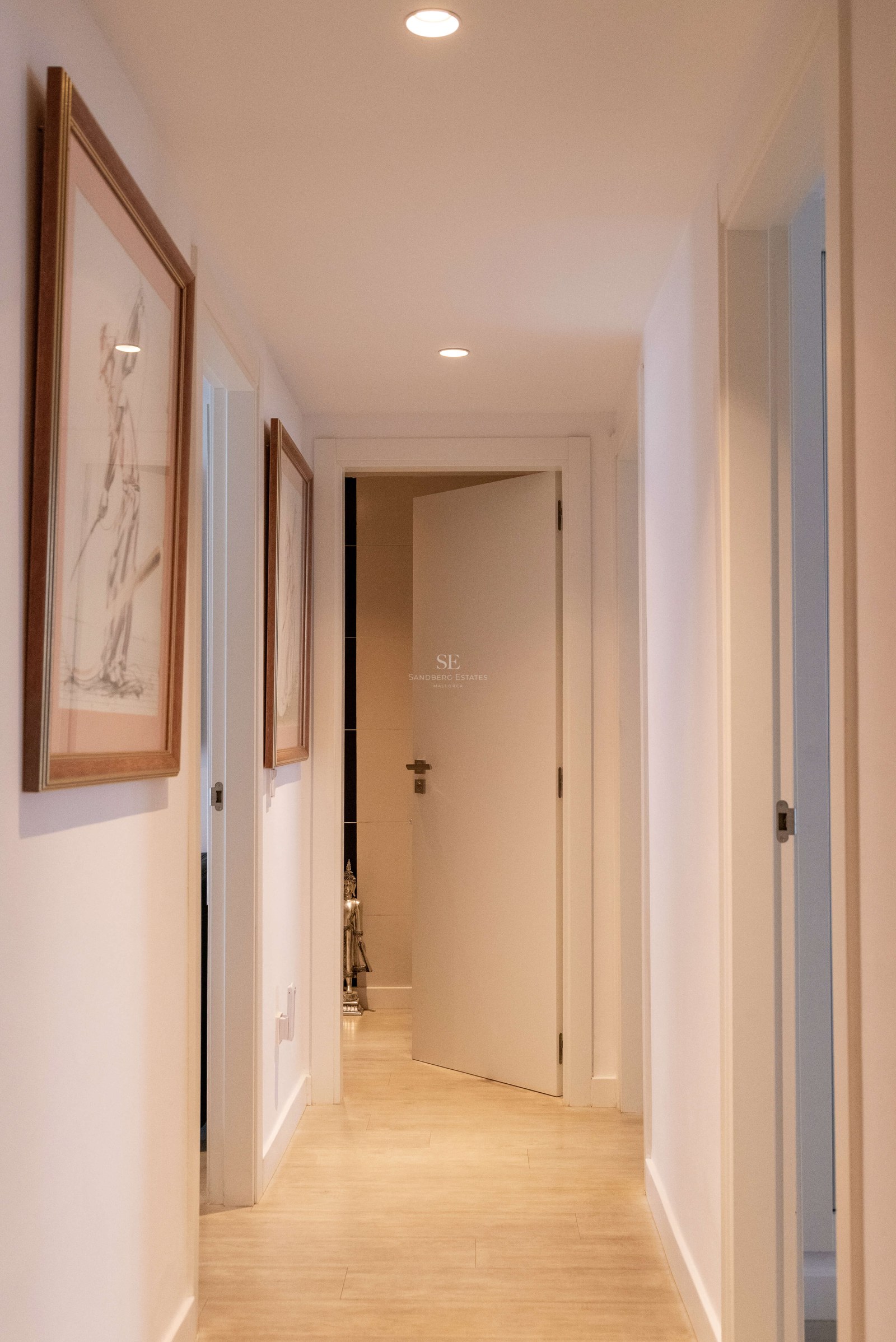 Couloir moderne aux murs blancs avec éclairage encastré et sol en bois clair menant à une porte ouverte.