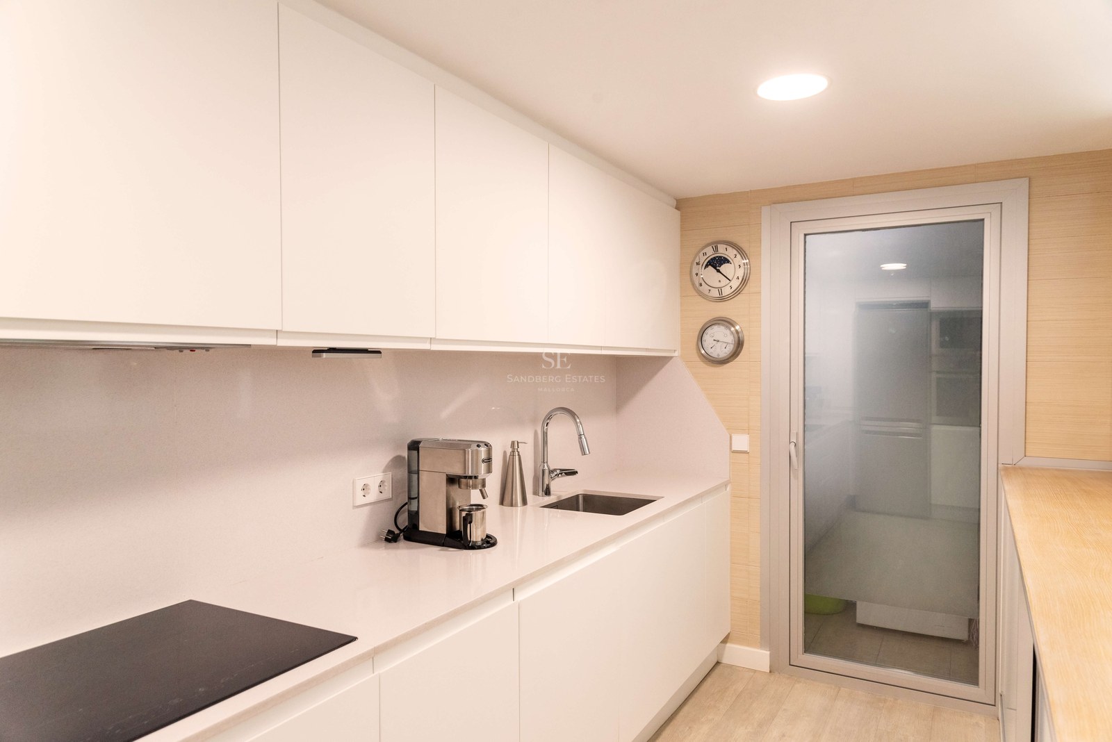 Cuisine moderne blanche avec placards sans poignées, plan de travail en quartz et porte vitrée.