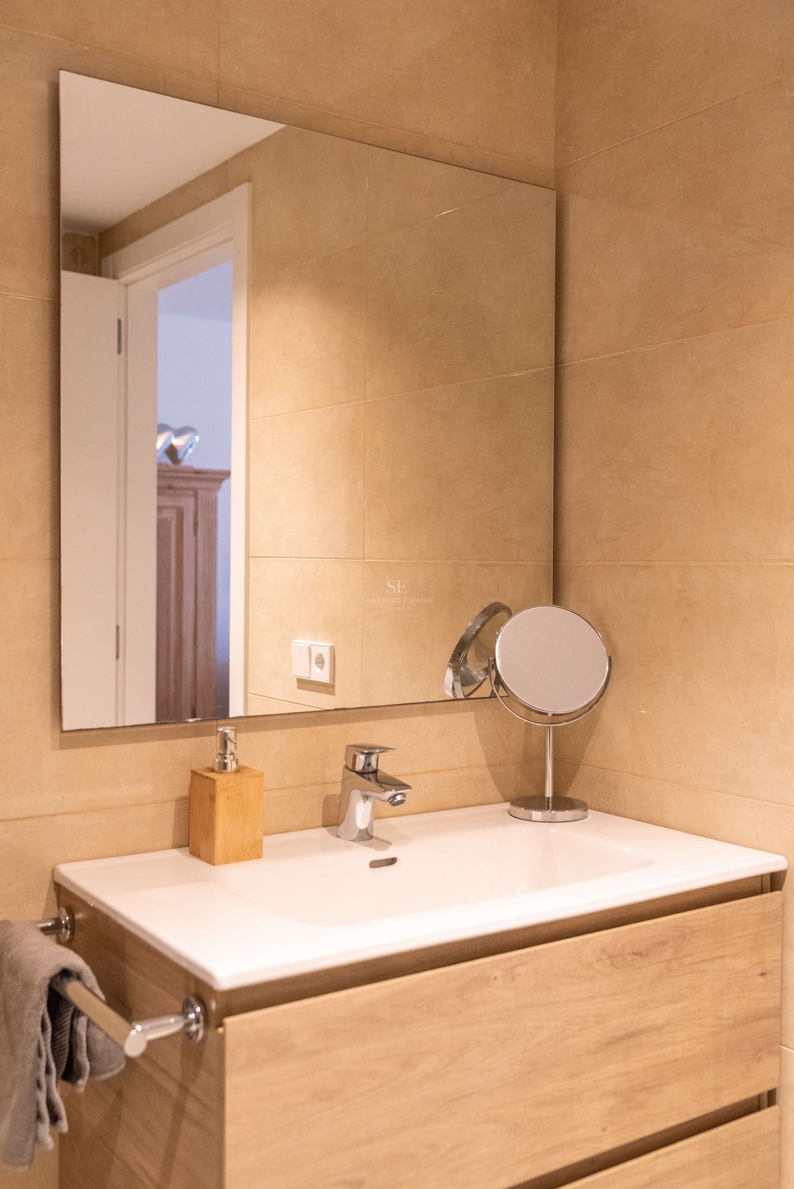 Vasque en céramique blanche sur meuble en bois clair, grand miroir et carrelage mural beige.