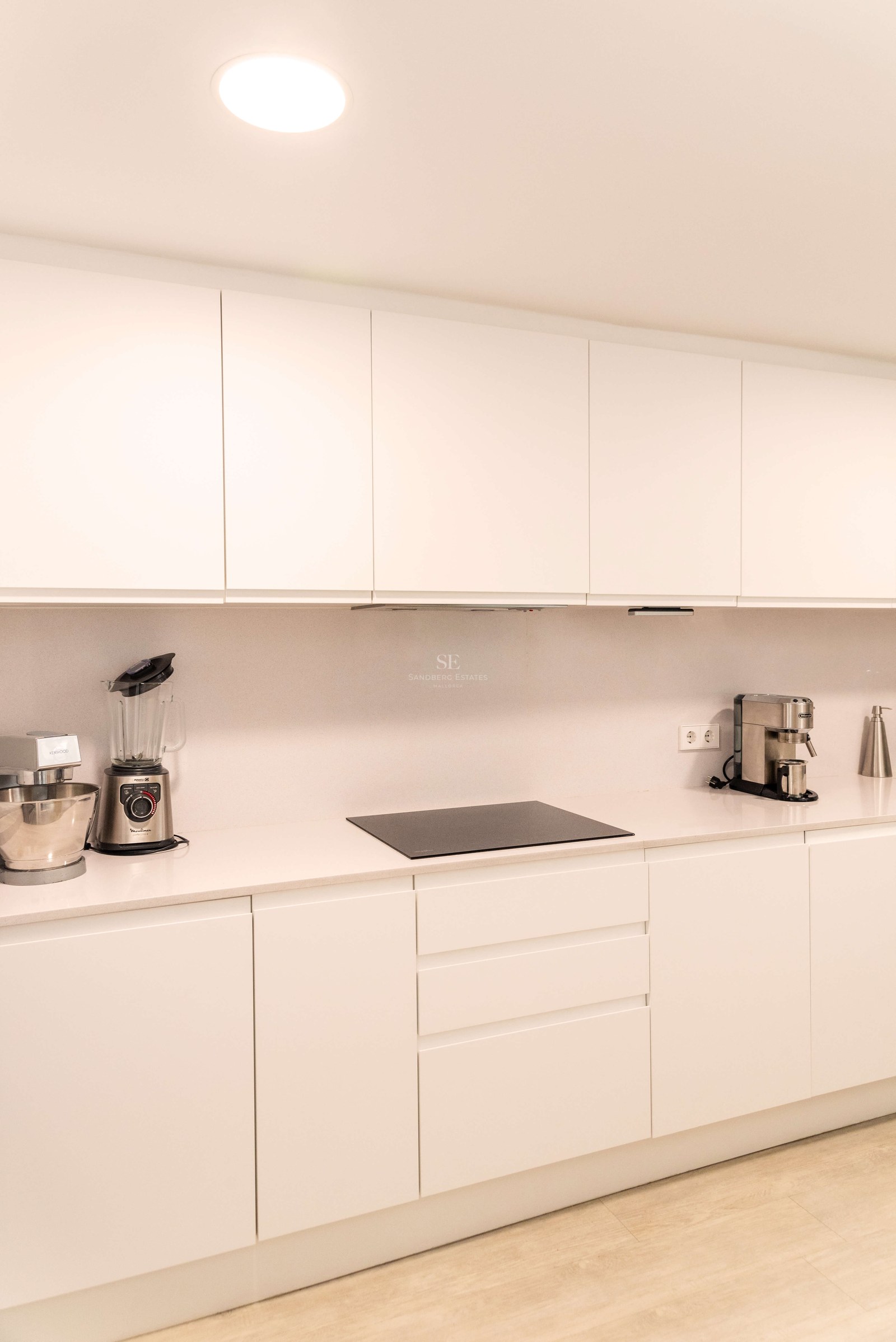 Cuisine blanche contemporaine avec placards sans poignées, plan de travail en quartz et plaque à induction.