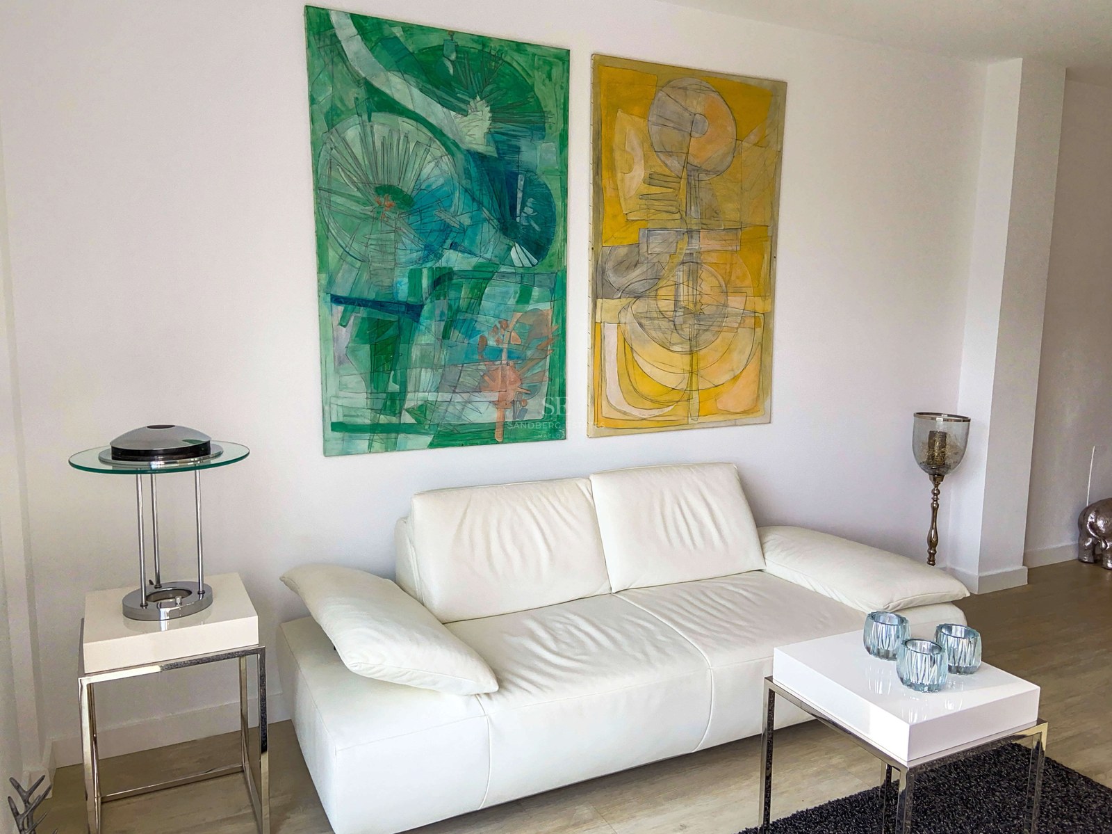 Canapé en cuir blanc avec peintures abstraites vertes et jaunes et mobilier minimaliste en chrome.