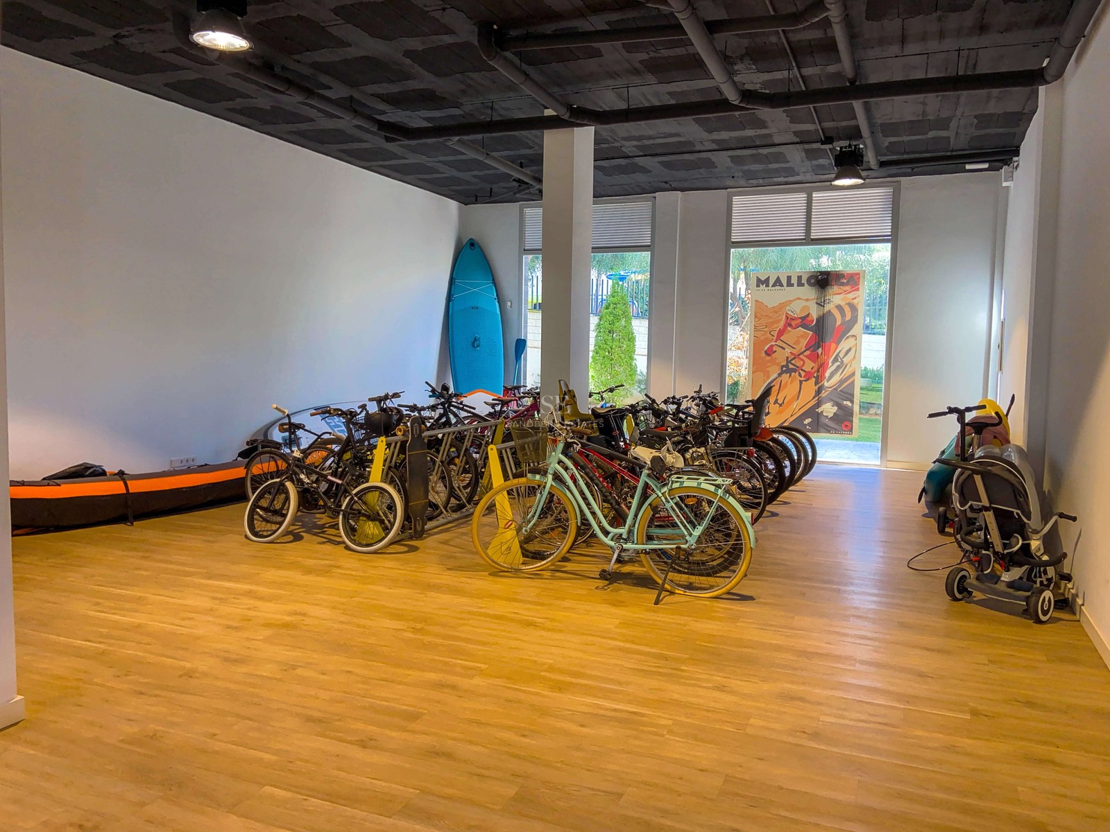 Grand espace de stockage intérieur avec vélos, planches de paddle et kayak sur sol en bois, style industriel.